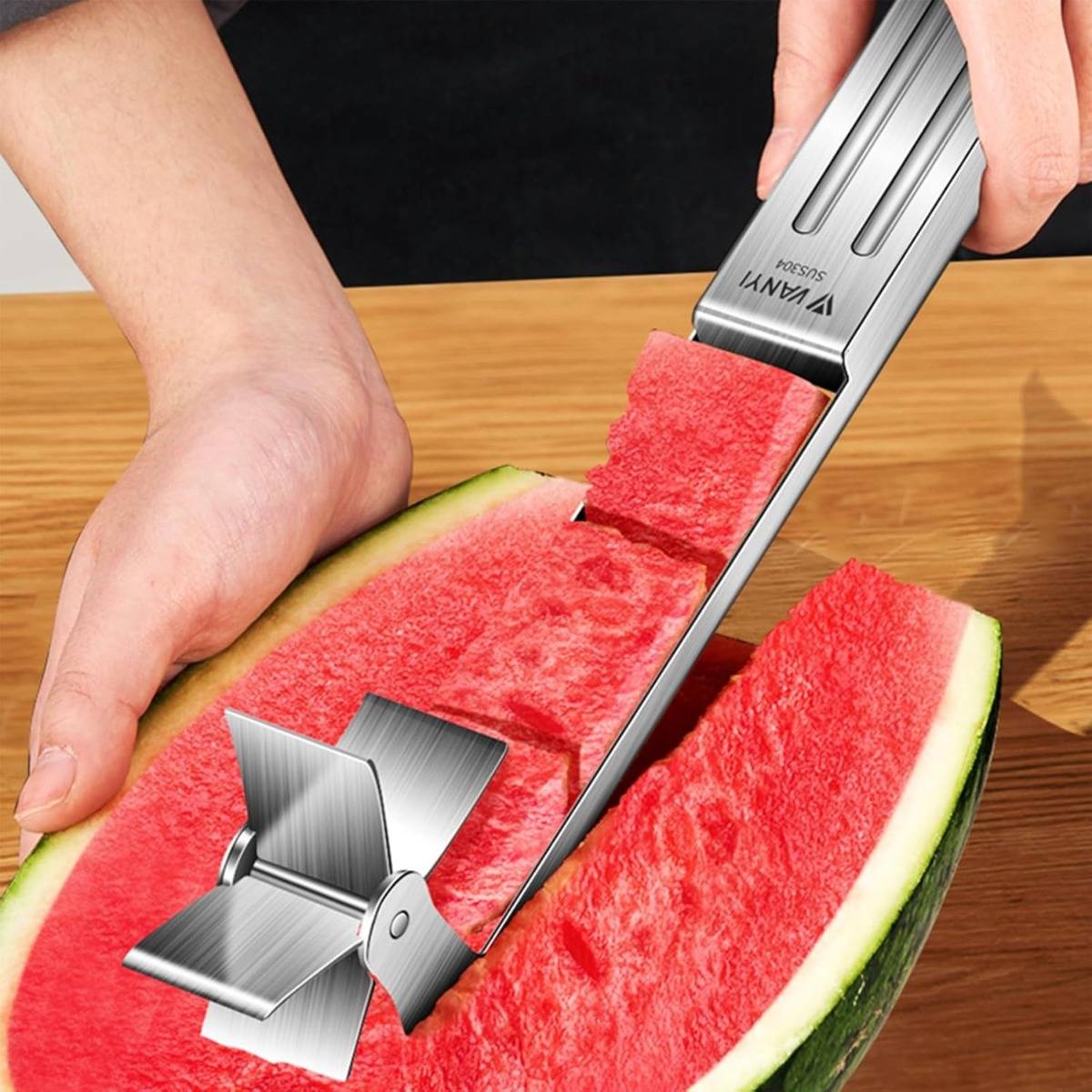 Hände, die ein Wassermelonenschneider- und Gabelwerkzeug verwenden, um einen langen Streifen Wassermelone von einer halbierten Melone auf einem Tisch zu schneiden und zu heben.