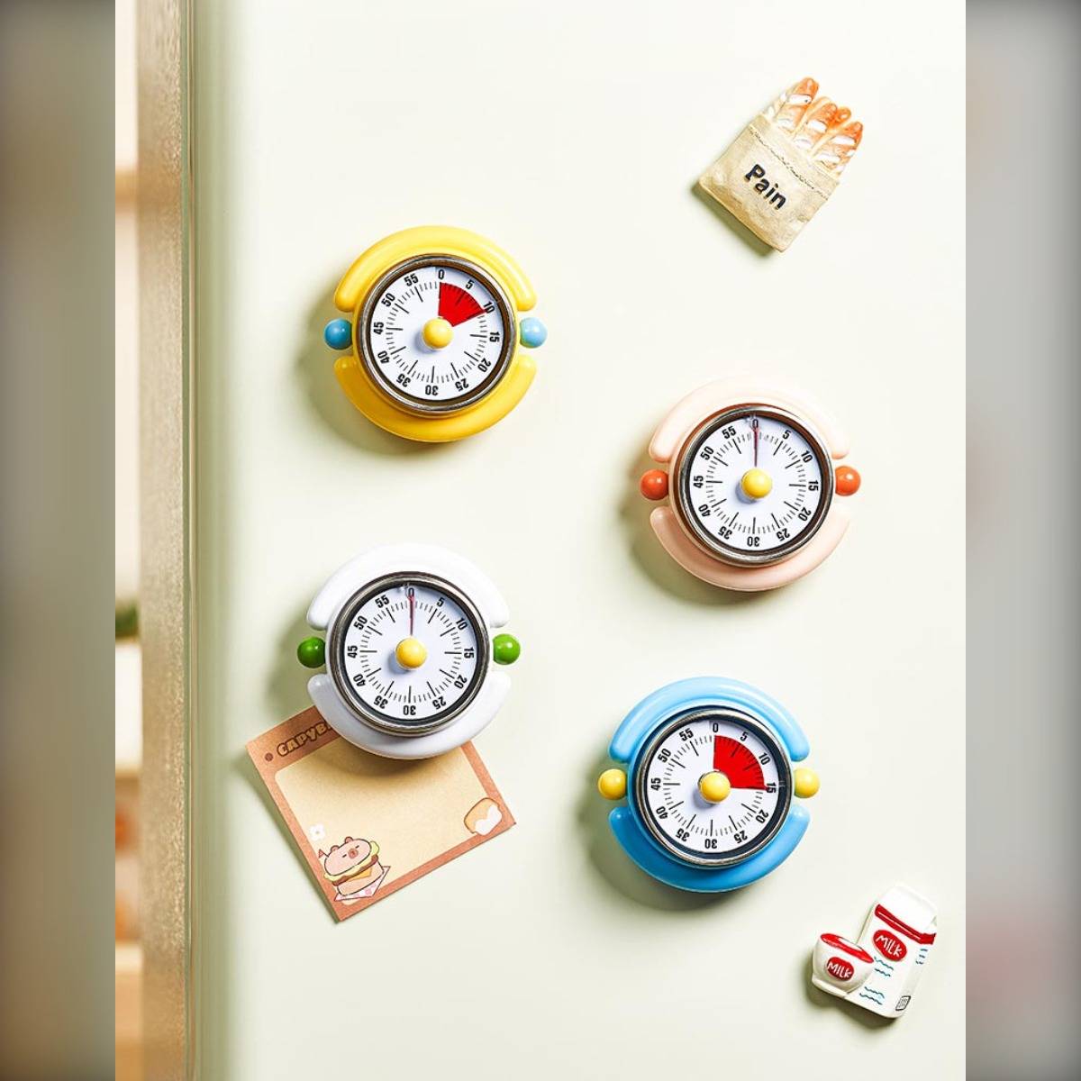 Vier bunte Küchentimer, die magnetisch an einem Kühlschrank befestigt sind, mit einem Notizzettel, auf dem 