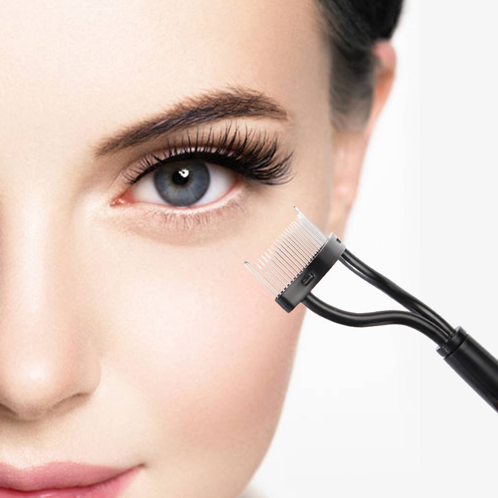 Nahaufnahme eines Frauengesichts mit einem sichtbaren Auge, während sich eine Kosmetikbürste mit kammartiger Spitze dem Augenbrauen-/Wimpernbereich nähert.