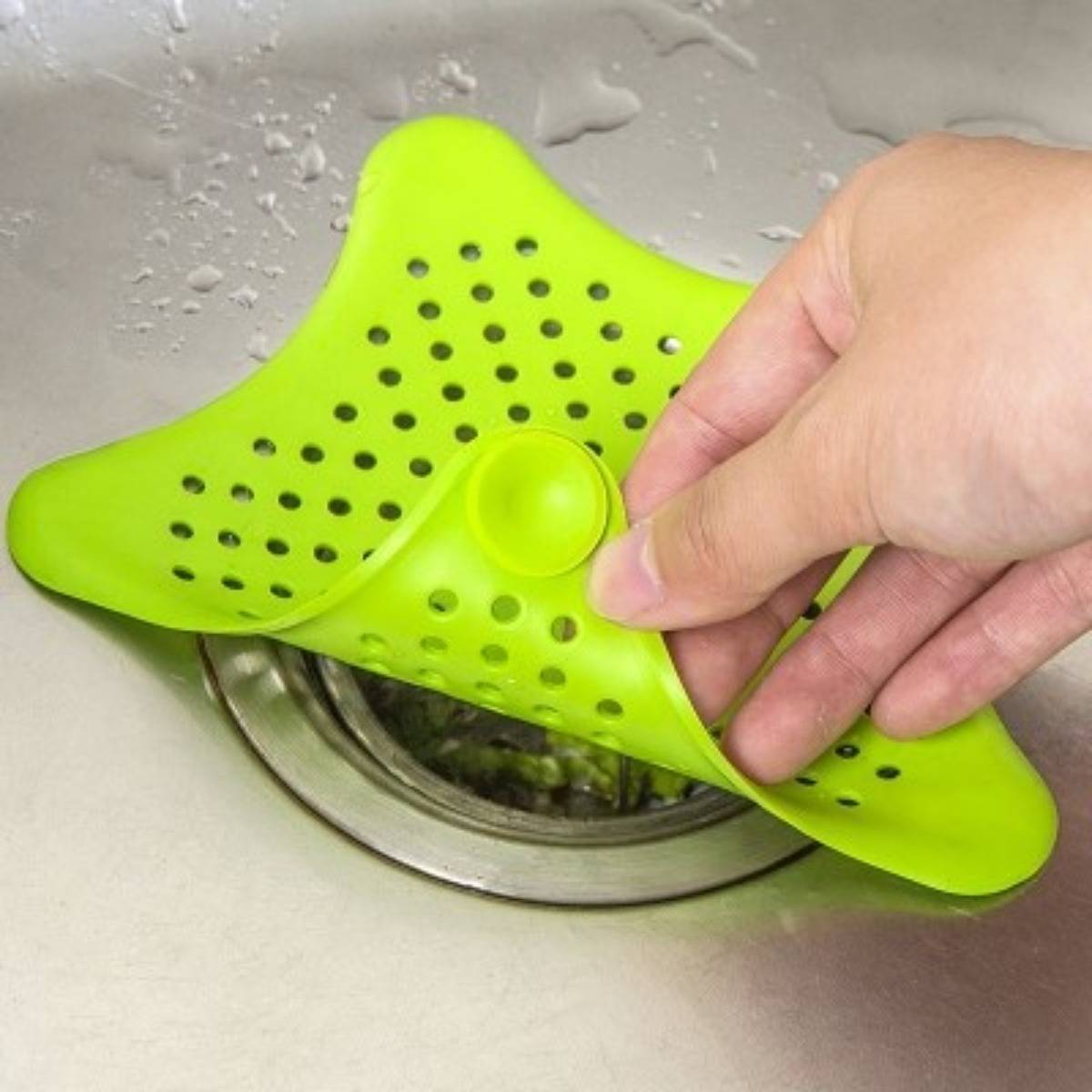 Eine Hand hält ein grünes Silikon-Spülbeckensieb über einen Küchenabfluss, das Verschmutzungen auffängt, während Wasser durch die Löcher abfließt.