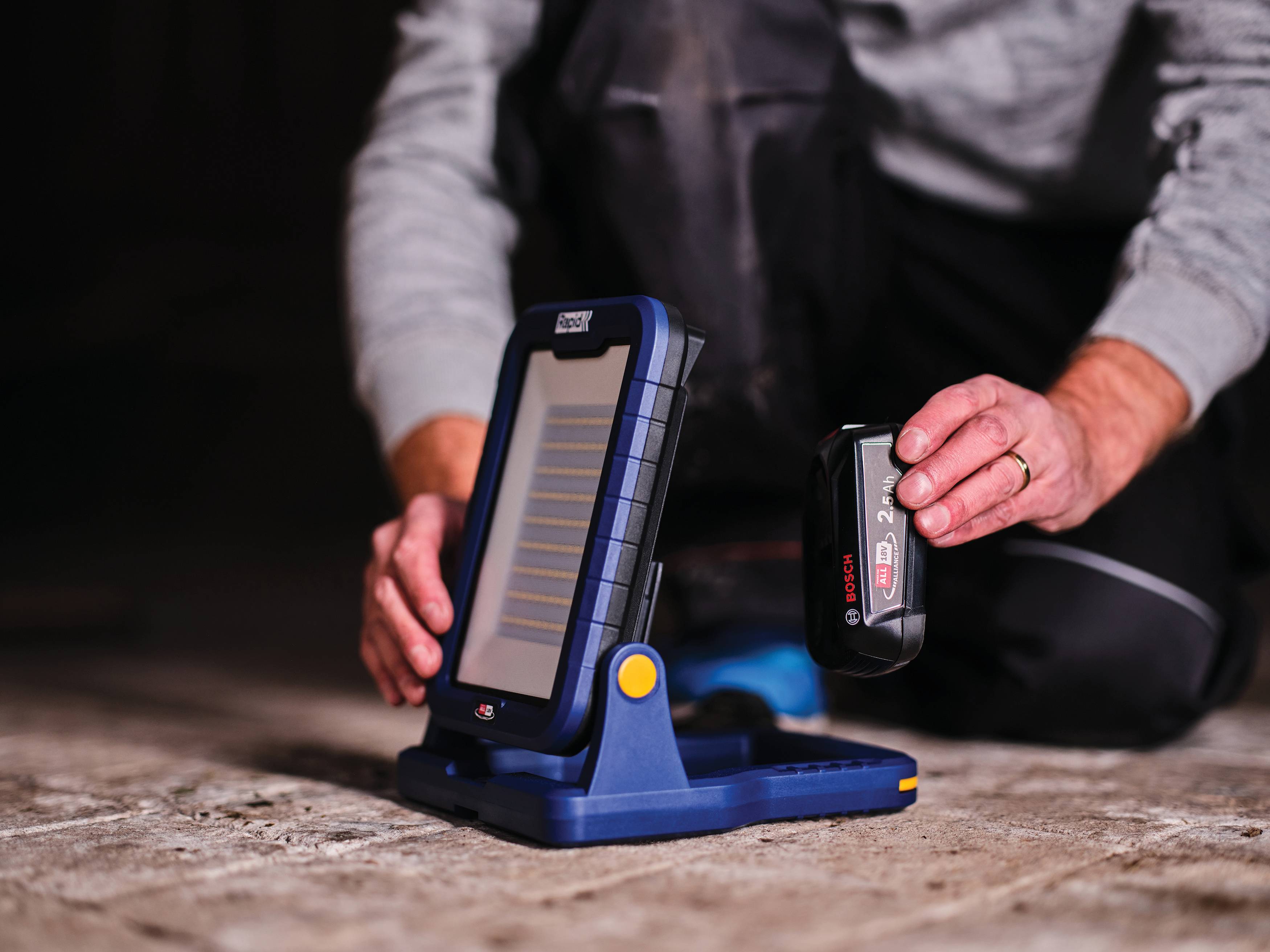 Eine Person kniet neben einem tragbaren solarbetriebenen Gerät und hält ein wiederaufladbares Batteriepaket in der Nähe seines Docks.