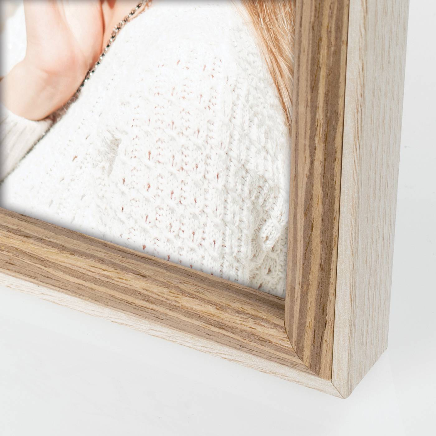 Nahaufnahme einer Ecke eines Holzbilderrahmens um ein unscharfes Foto einer Person in einem weißen Pullover.