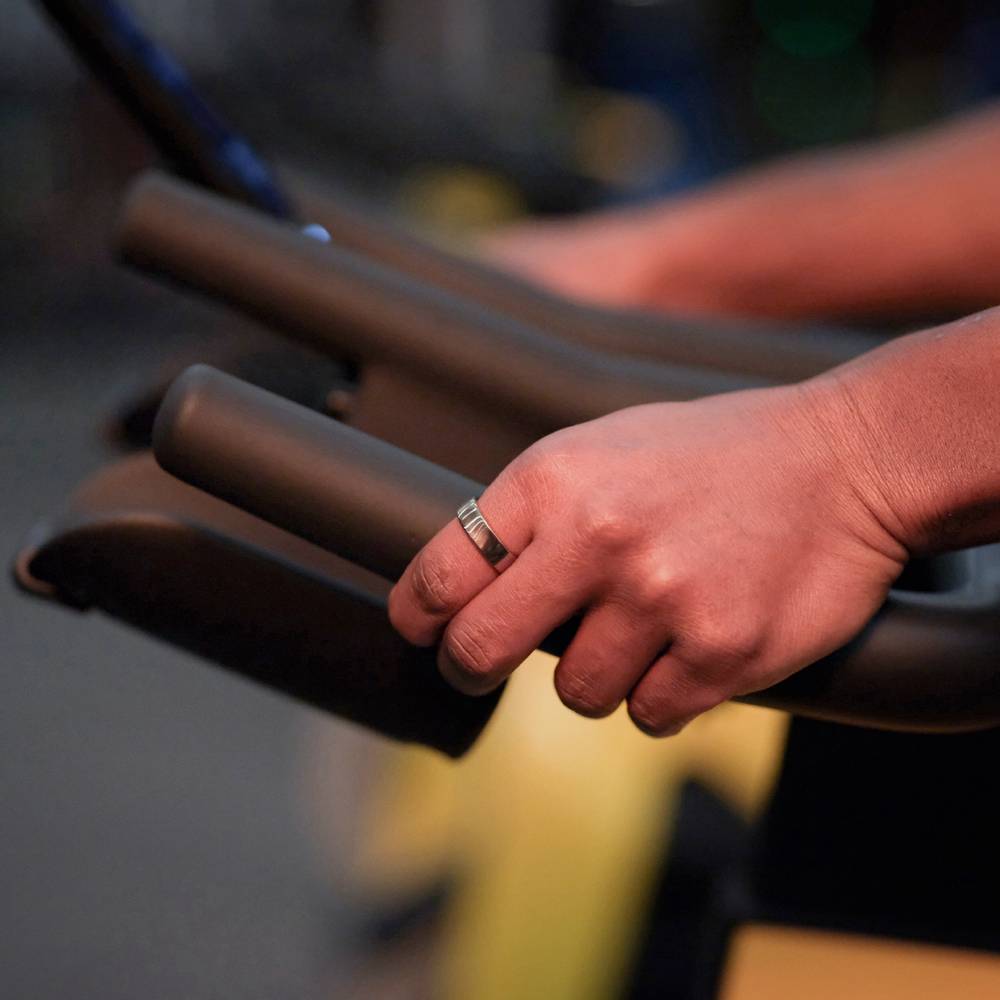 Nahaufnahme einer Hand mit einem Ring, die einen dunklen Trainingsgerätehalte in einem Fitnessstudio umgreift.