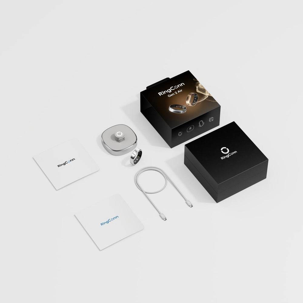 RingConn intelligenter Ring mit Verpackung und Zubehör auf weißem Hintergrund angeordnet, einschließlich zwei Kartons, eines Ladeetuis, eines Rings, eines Kabels und von Broschüren.