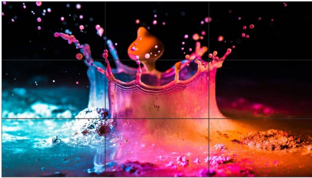 Farbenfrohe Flüssigkeit spritzt in einer Kronform nach oben, mit rosa, orange und blauem Farbspritzer, der gegen einen dunklen Hintergrund aufprallt.