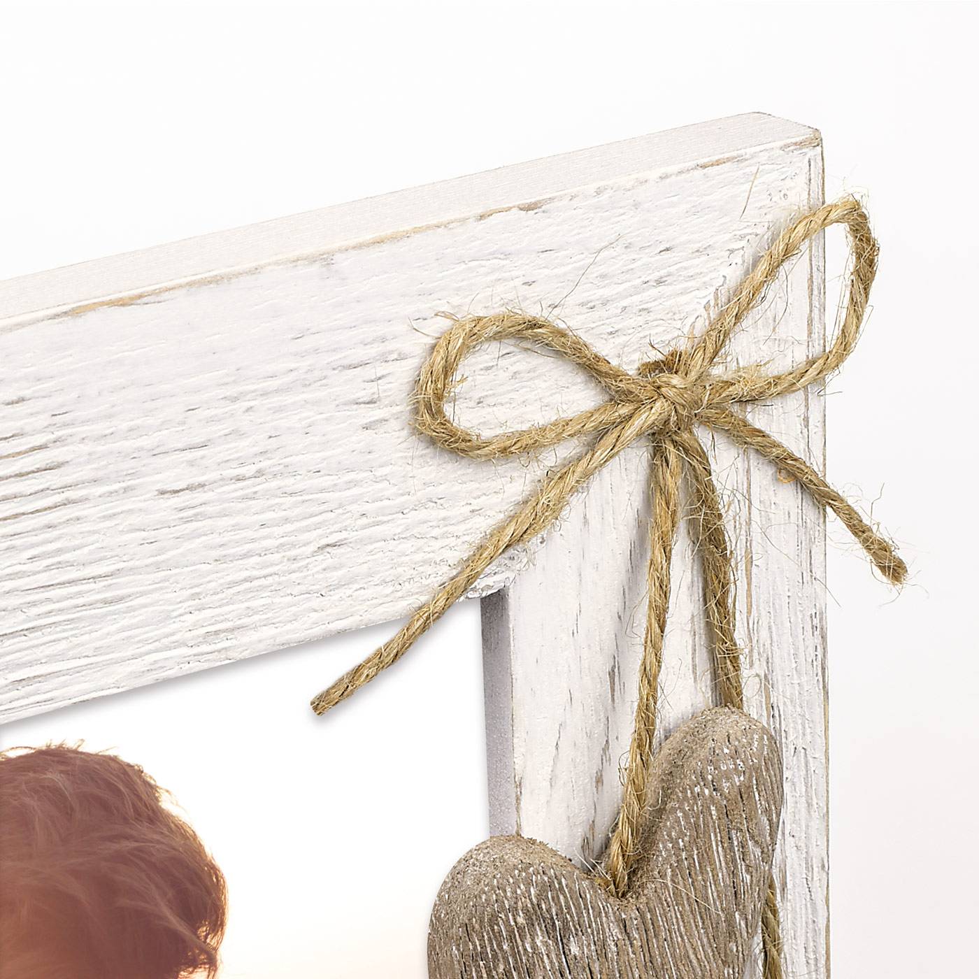 Nahaufnahme einer weißen abgenutzten Holzrahmenecke mit einer Schnurbinde und einem hängenden Herzornament.