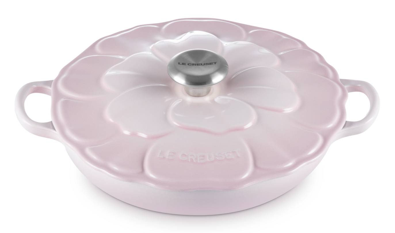 Hellrosa gusseiserner Bräter von Le Creuset mit blütenförmigem Deckel und silbernem Knauf, dargestellt vor weißem Hintergrund.
