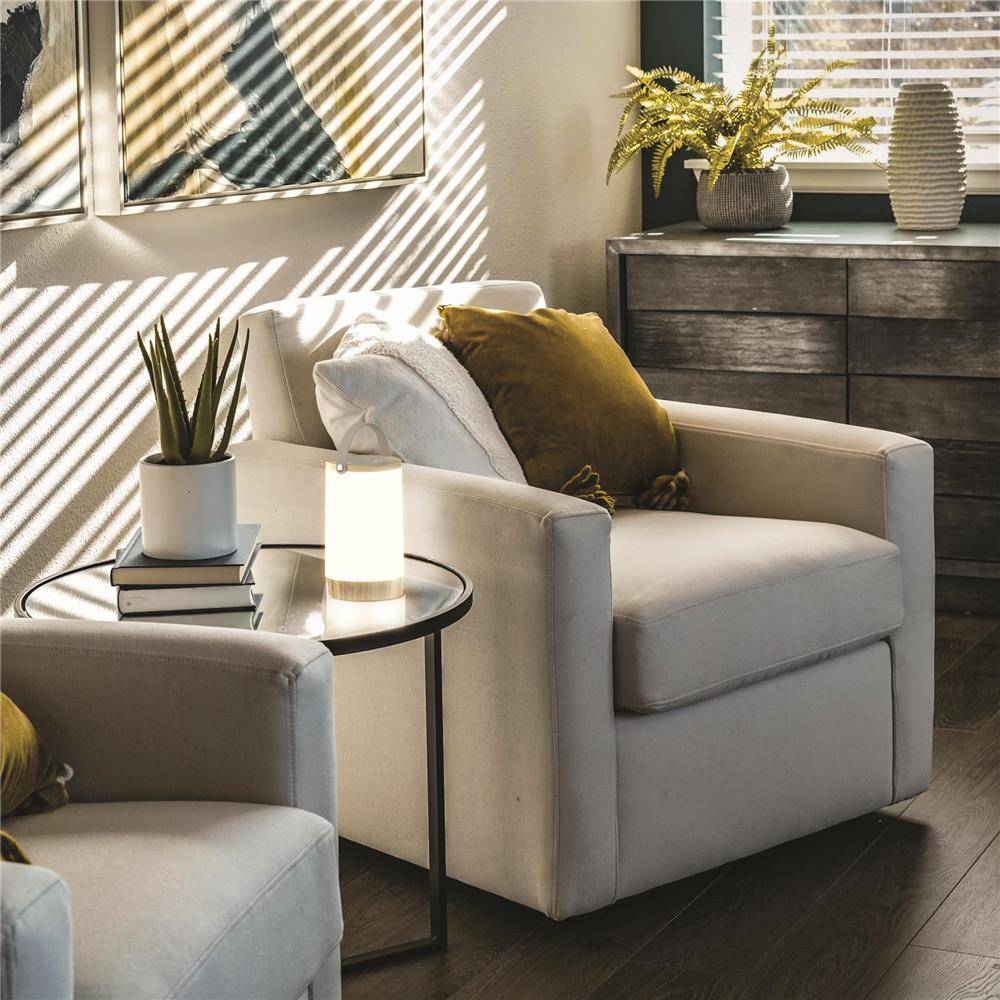Modernes Wohnzimmer mit beigen Sesseln, rundem Beistelltisch, Pflanzen und Sonnenlicht, das gestreifte Schatten an die Wand und auf die Möbel wirft.