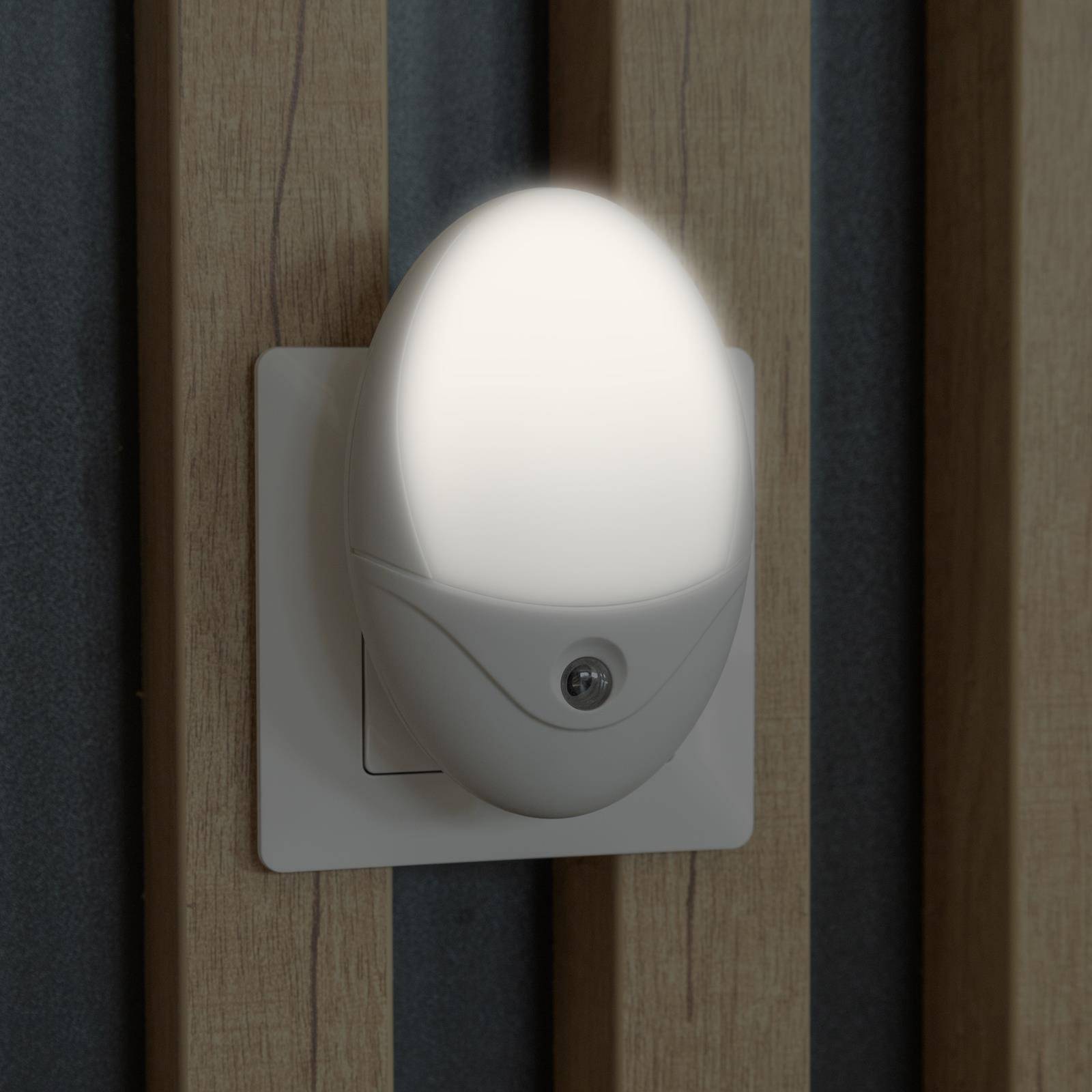 Ein an der Wand montiertes Bewegungsmelder-Nachtlicht leuchtet auf einer Schalterplatte zwischen Holzpaneelen.