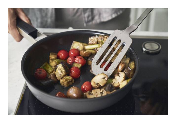 Gemüse und Kirschtomaten werden in einer Bratpfanne auf einer Kochplatte sautiert und mit einem Spatel gerührt.