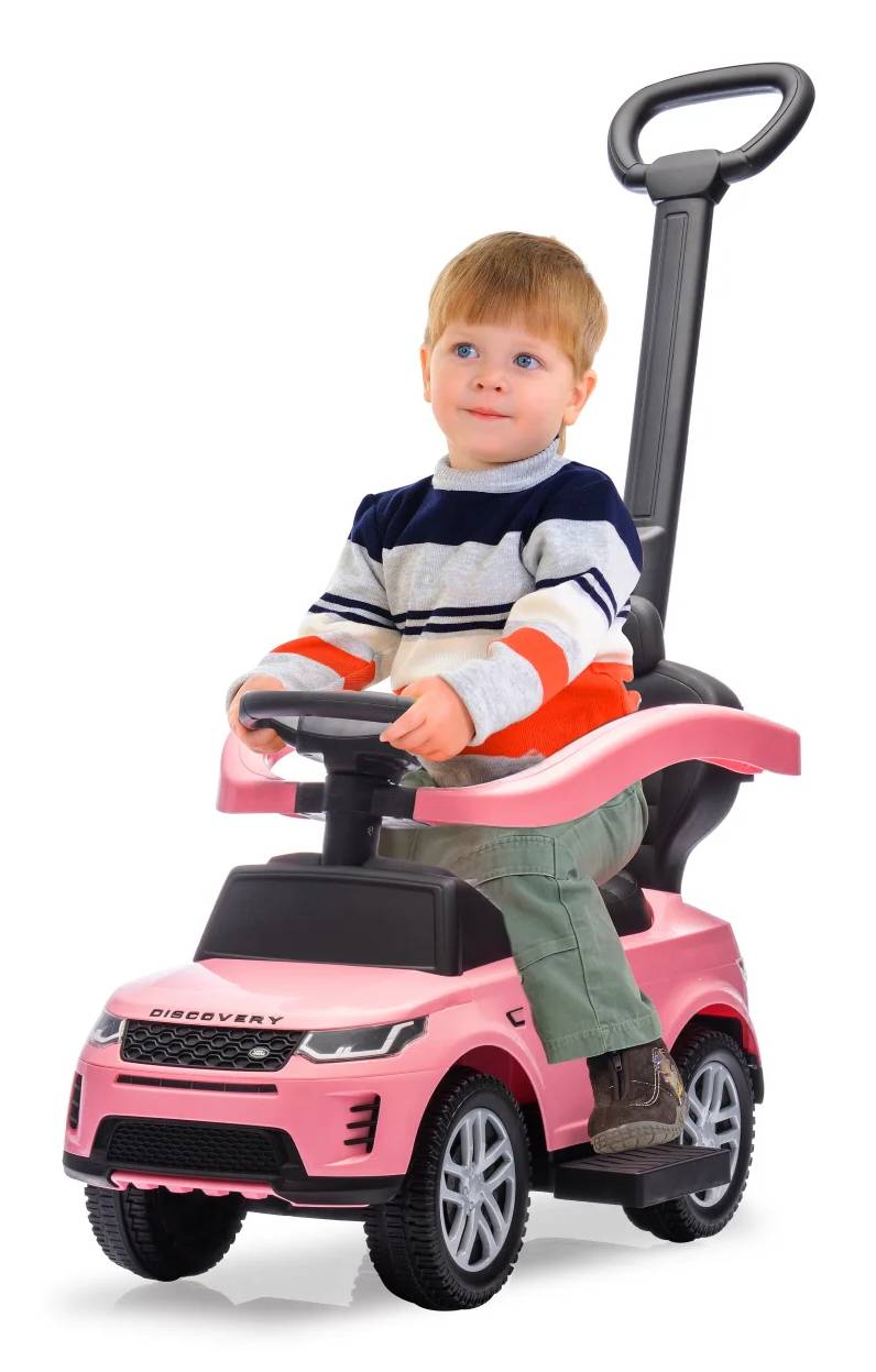 Kleines Kind, das auf einem rosa Rutschauto mit Schiebegriff sitzt, das Lenkrad hält und nach vorne schaut.