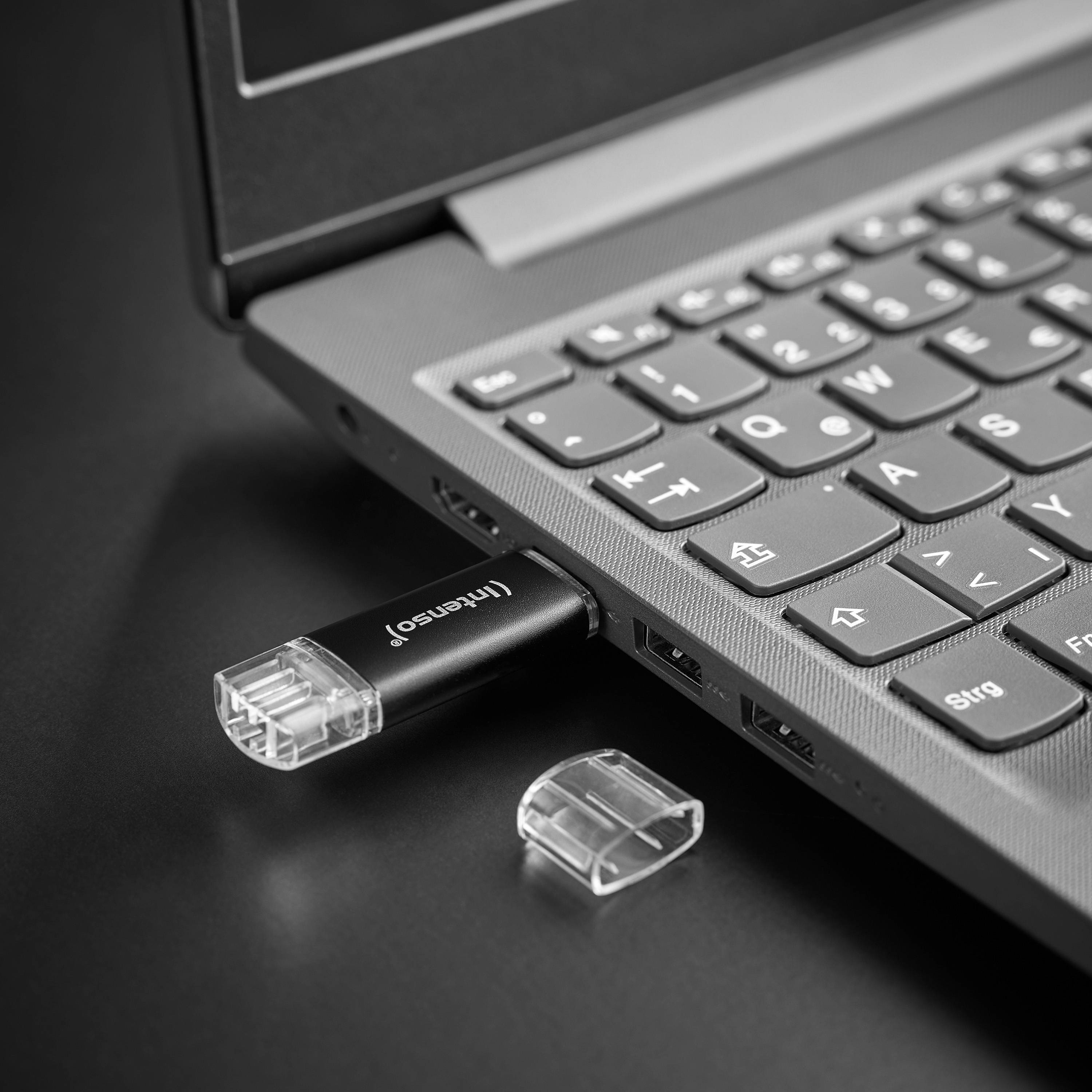 USB-Stick in die Seite eines Laptops eingesteckt, mit seiner transparenten Kappe daneben auf einer schwarzen Oberfläche liegend.