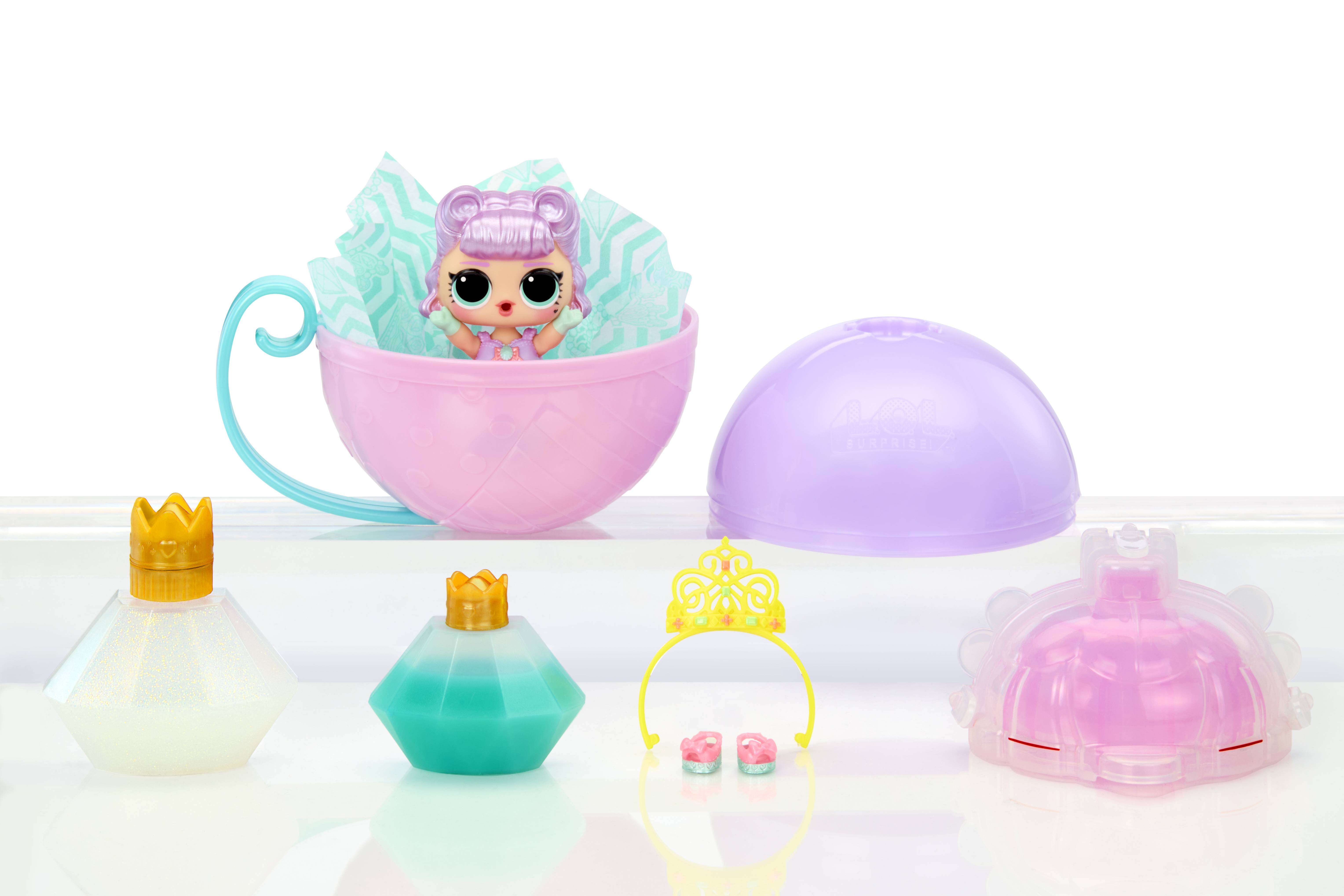 Spielzeugpuppe mit Zubehör auf einer weißen Oberfläche angezeigt: eine kleine Puppe in einer rosa-mintgrünen Teetasse, eine violette Kapsel, zwei kleine Kronen und drei kunststoffähnliche Flaschenteile.