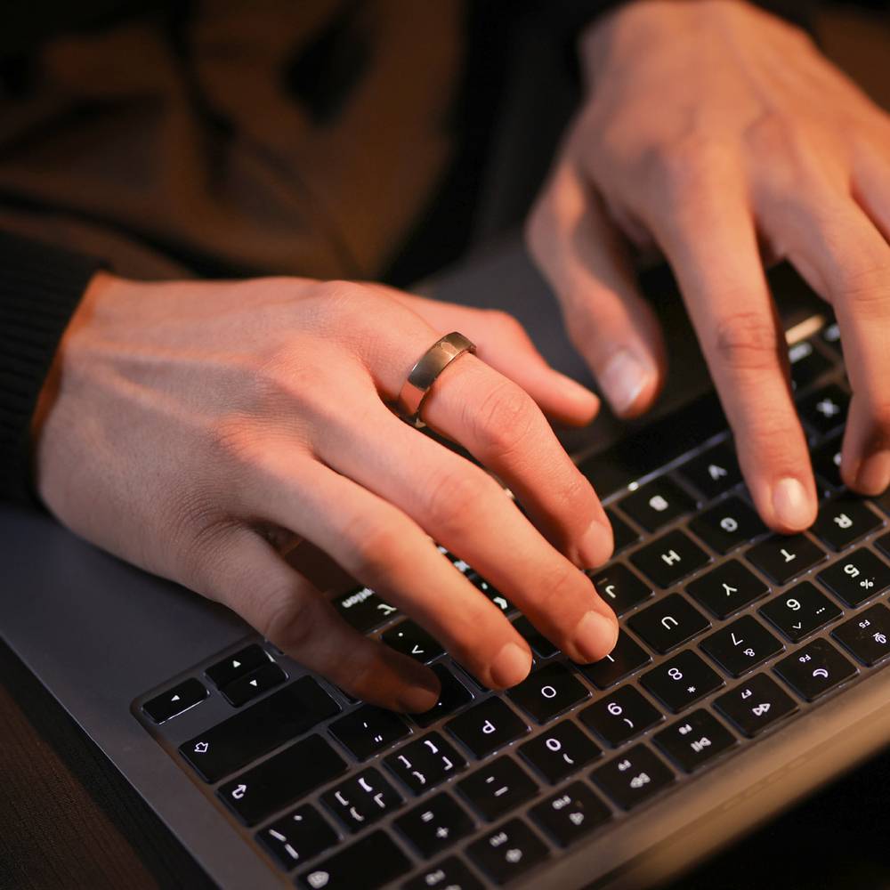 Nahaufnahme von Händen, die auf einer Laptop-Tastatur tippen, wobei ein Finger Tasten drückt und an einer Hand ein Ring zu sehen ist.