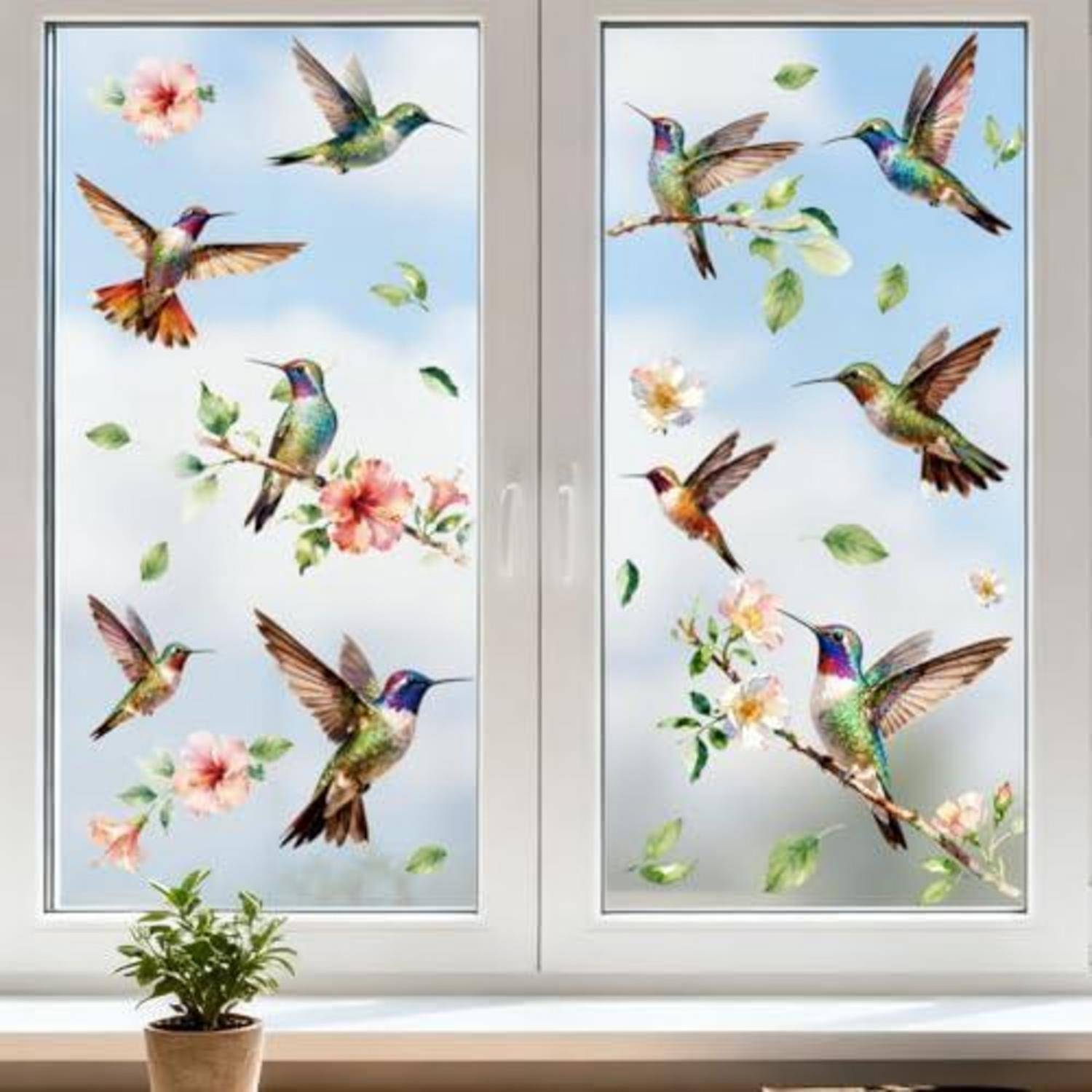 Dekoratives Fensteraufkleber mit bunten Kolibris, Blumen und Blättern auf einem zweiteiligen weißen Fenster über einer kleinen Topfpflanze.