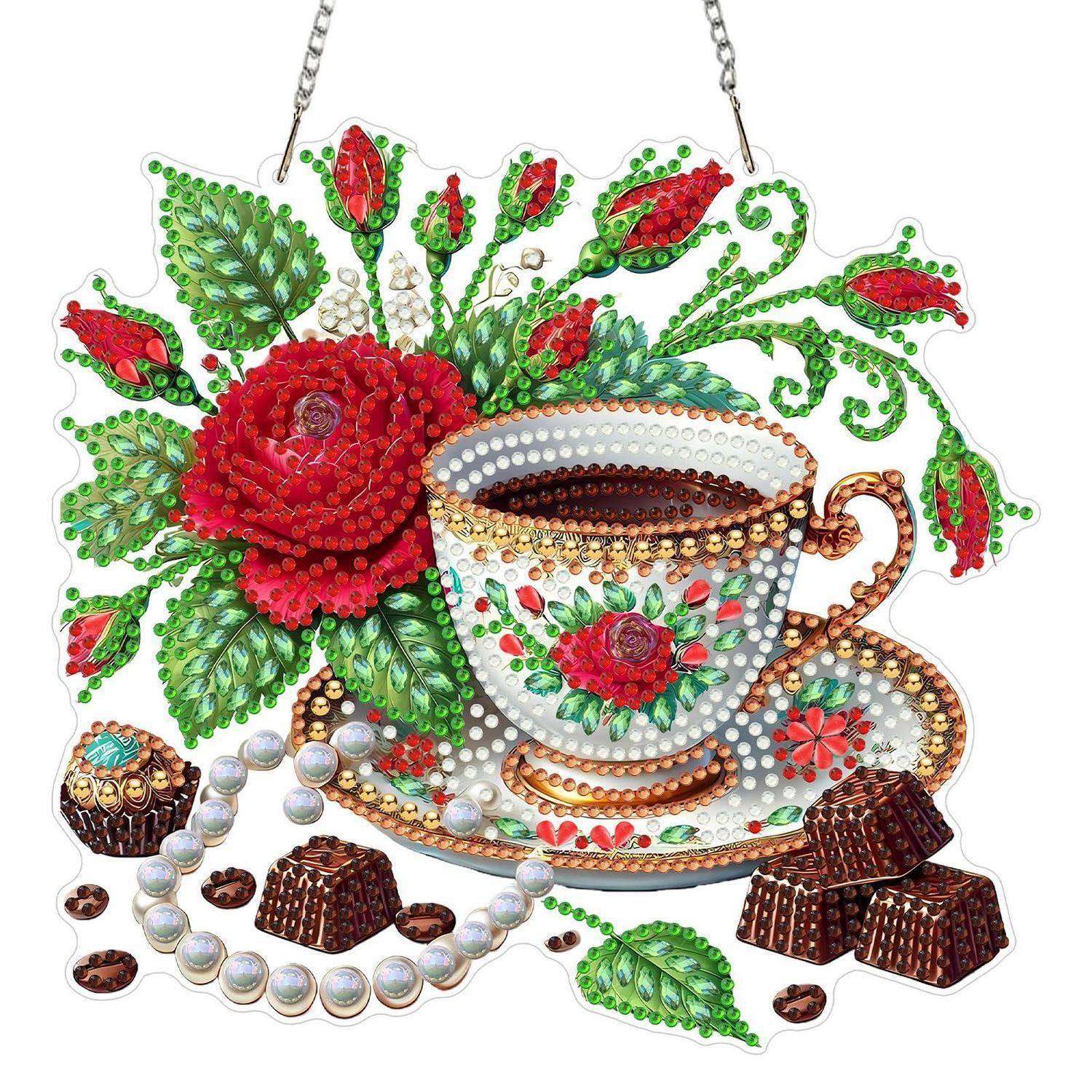 Perlengeschmuck einer Teetasse und Untertasse mit roten Blüten, grünen Blättern, Pralinen und Perlmuschperlen, aufgehängt an Ketten.