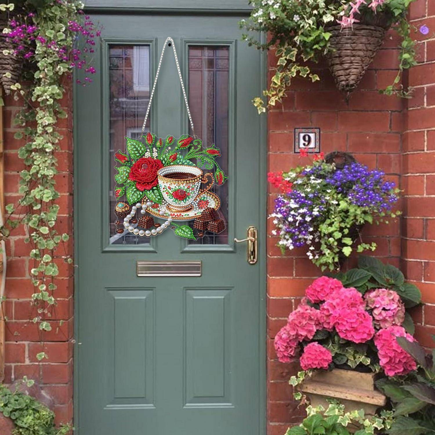 Dekorierte grüne Haustür mit Blumenkranz, umgeben von hängenden und getopften Blumen an einem Hauseingang aus Ziegelsteinen, Nummer 9 sichtbar.