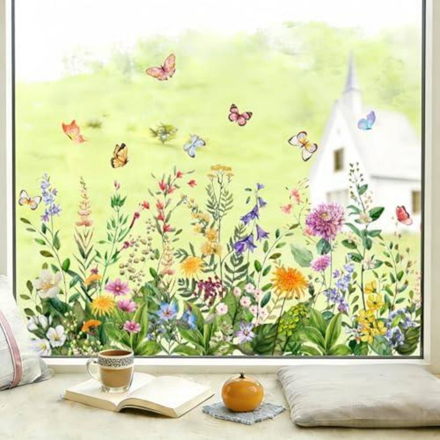 Ein gemütlicher Fensterplatz mit einem aufgeschlagenen Buch, Tee und Kissen überblickt einen im Malstil gehaltenen Garten mit bunten Wildblumen und Schmetterlingen, wobei eine weiße Kirche im Hintergrund zu sehen ist.