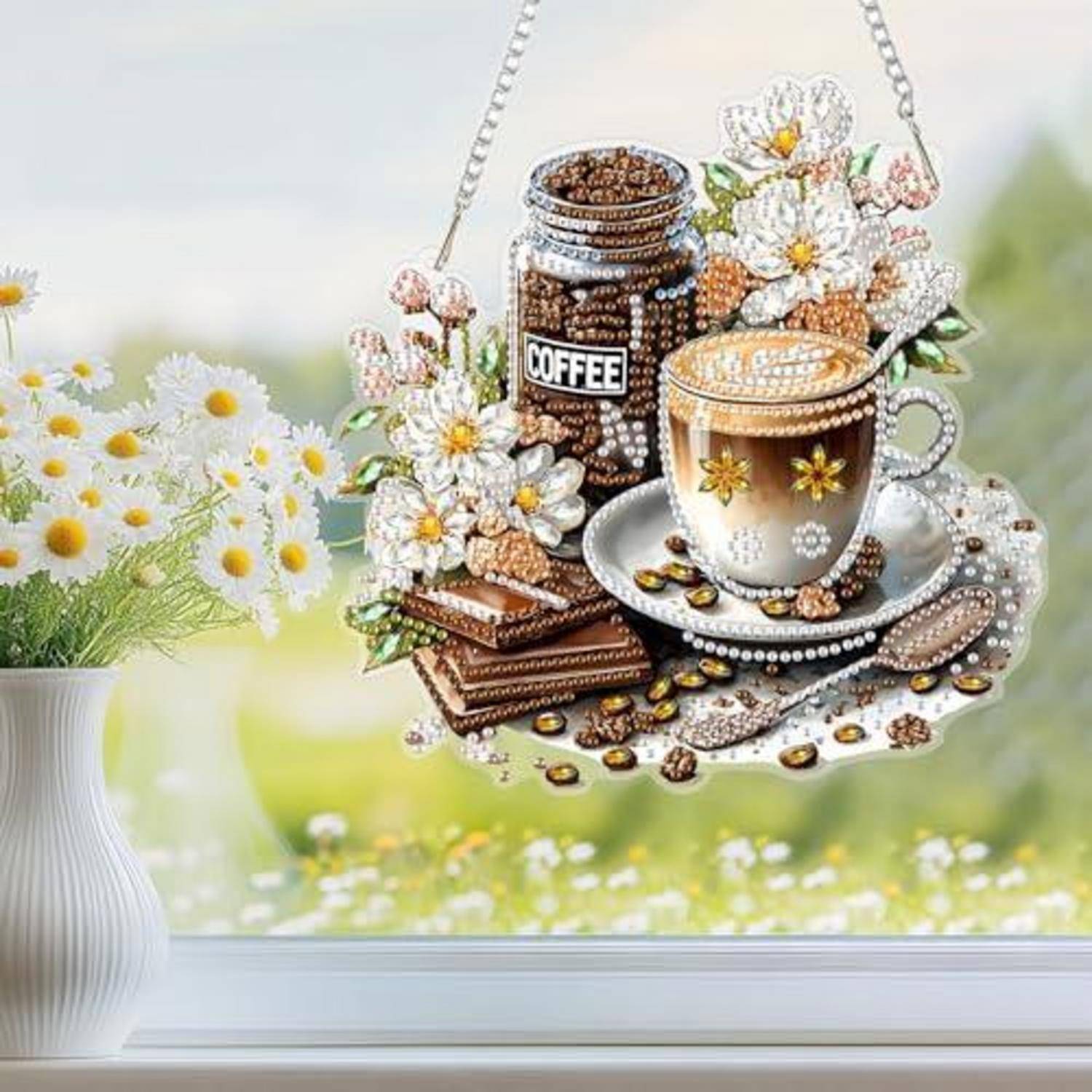 Dekoratives Kaffee-Thema-Hängekristall mit einer Perlen-Kaffeeflasche, Tasse, Untertasse, Blumen und verstreuten Bohnen neben einer Vase mit Gänseblümchen.