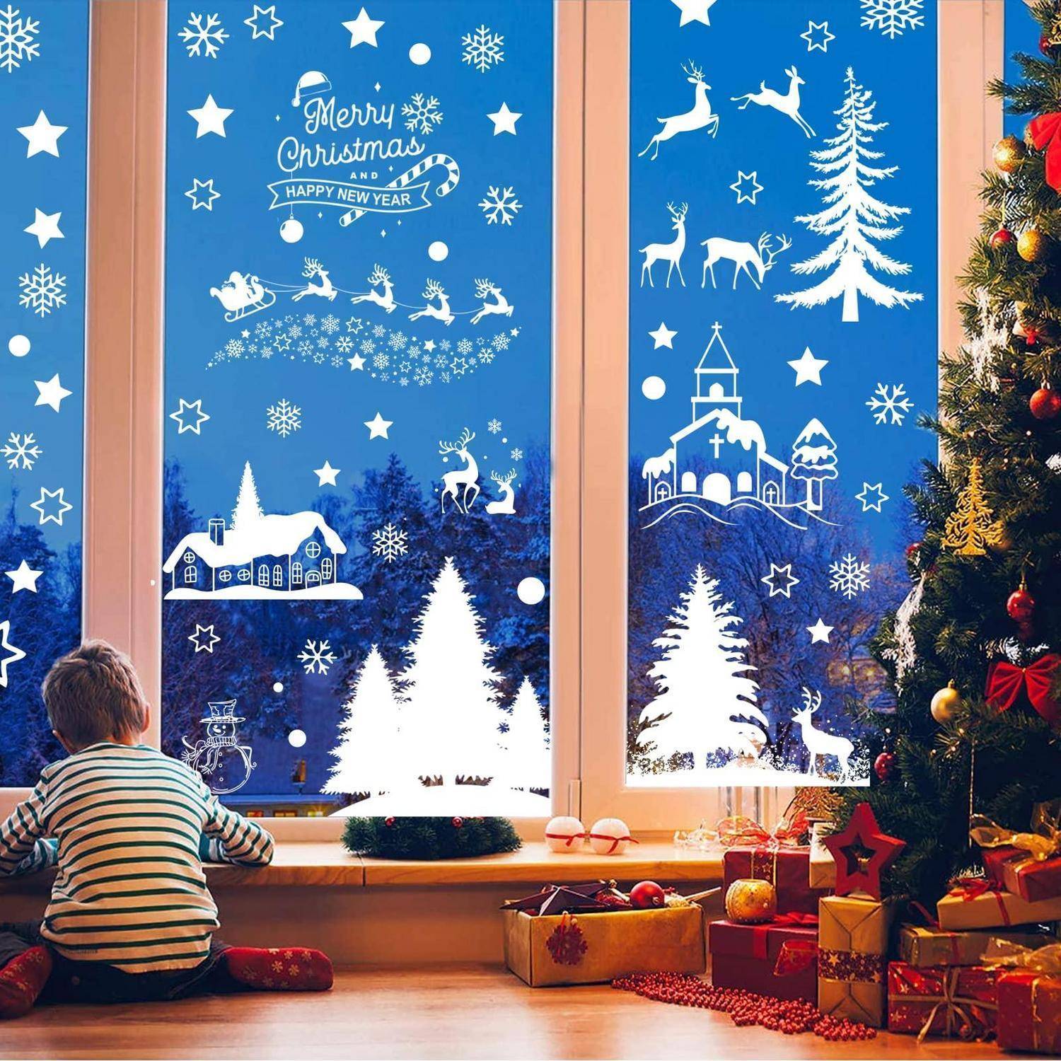 Kind sitzt am Fenster und schaut sich Weihnachtsfensteraufkleber an: „Frohe Weihnachten Glückliches Neues Jahr