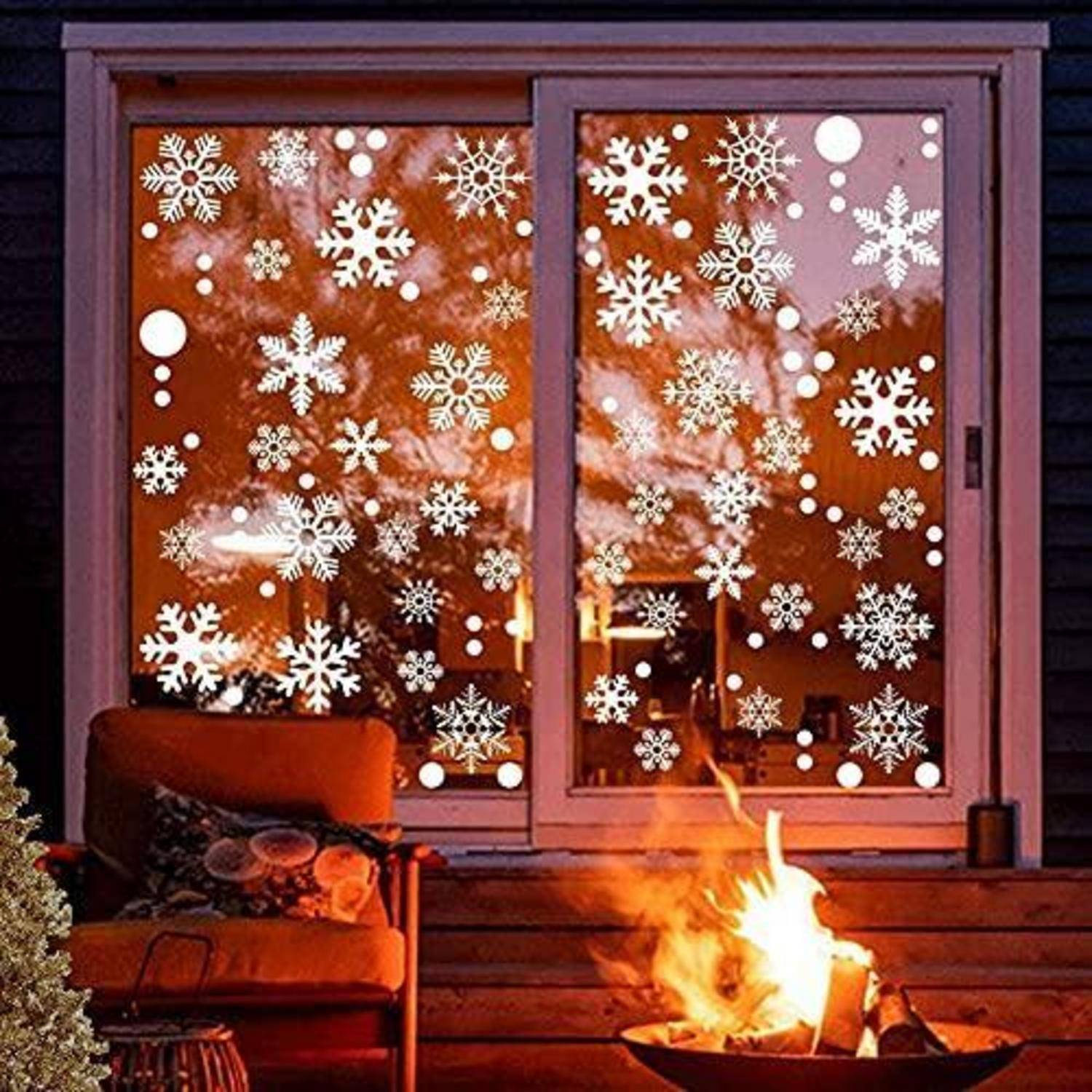 Gemütliche Veranda mit brennender Feuerschale und Lehnstuhl vor einem Fenster, das mit weißen Schneeflocken-Aufklebern verziert ist, was auf Winter- oder Feiertagsdekoration hindeutet.