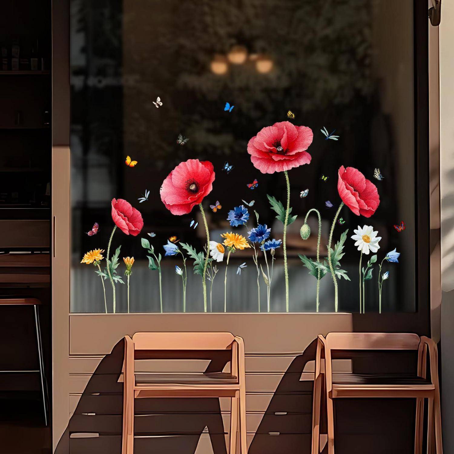 Schaufenster mit farbenfrohen bemalten Blumen und Schmetterlingen hinter zwei Holzstühlen im Sonnenlicht.