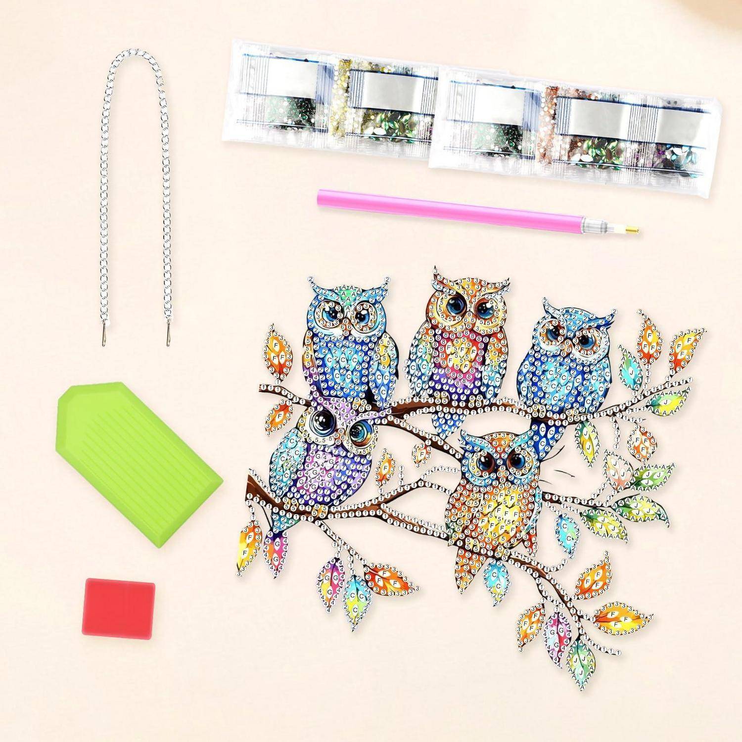 Diamond-Painting-Set mit Eulendesign, zeigt Werkzeugteile, Schalen, Stift, Kette und fertige bunte Eulenkunst auf Ästen.