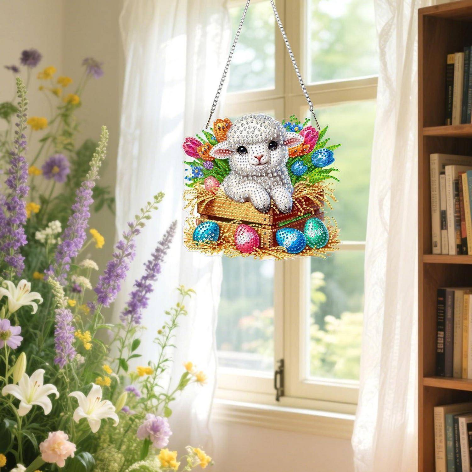 Dekoratives Oster-Hängeohrament mit einem geschmückten Lamm in einem Korb, umgeben von bunten Eiern und Blumen, neben einem hellen Fenster zur Schau gestellt.
