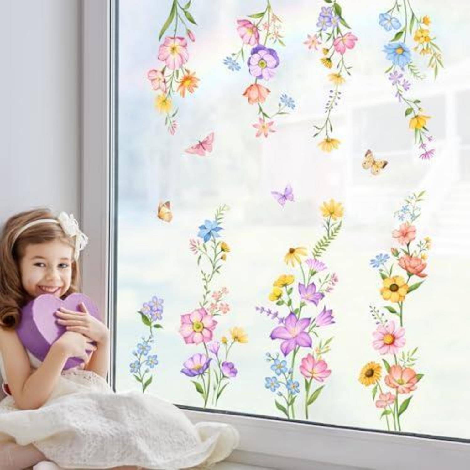 Lächelndes Mädchen mit einem violetten Herz sitzt neben einem Fenster, das mit farbenfrohen Blumen- und Schmetterlingsstickern verziert ist.