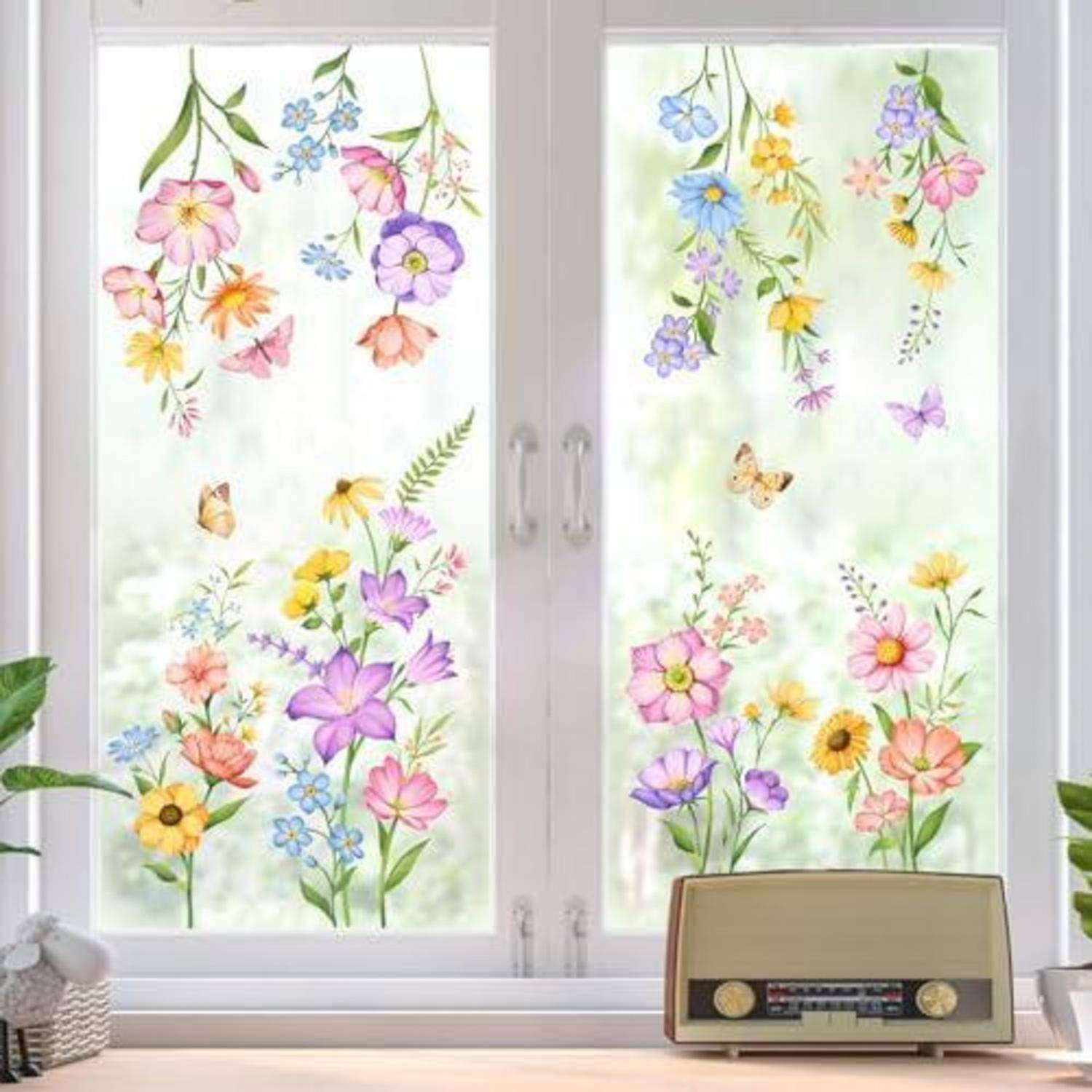 Gefrostetes Fenster mit farbenfrohen Blumen- und Schmetterlingsdekor; ein Vintage-Radio sitzt auf der Fensterbank darunter.