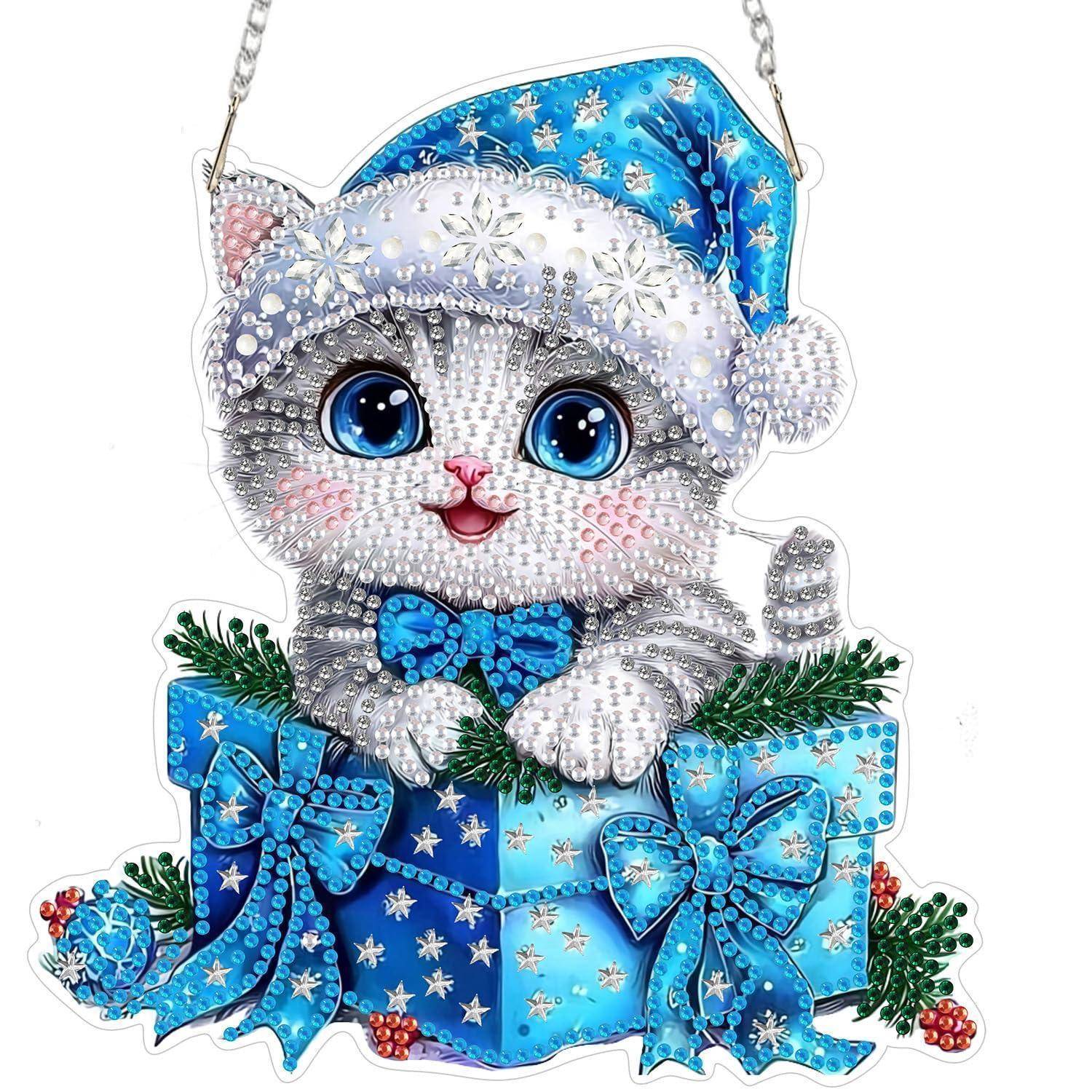 Ein juwelenbesetztes weißes Kätzchen-Ornament, das einen blauen Weihnachtsmütze trägt, sitzt in einer verpackten Geschenkbox mit Schleifen und festlichem Grün.