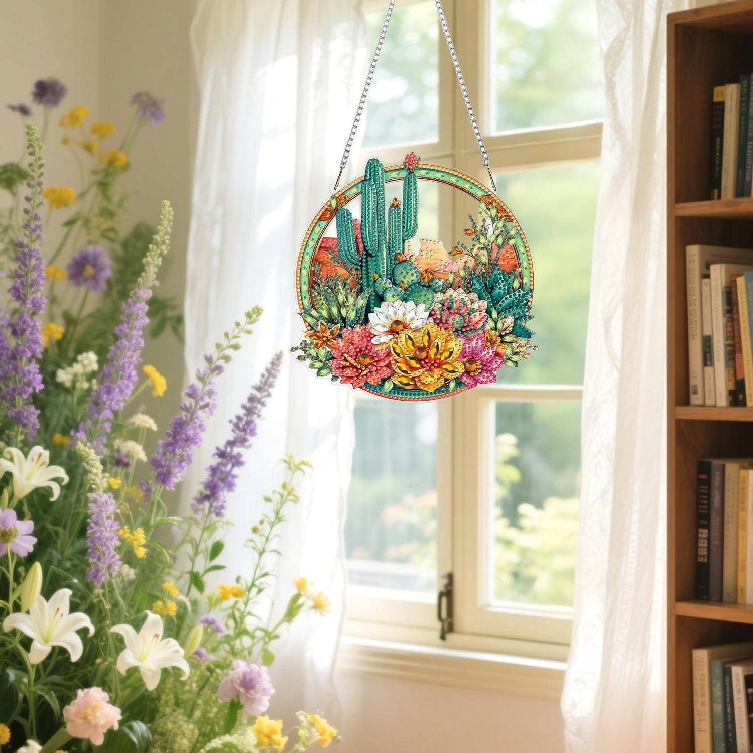Bunter Kaktus- und Blumen-Hängekristall an einem sonnigen Fenster, mit einer Blumenvase in der Nähe und einem Bücherregal im Zimmer.