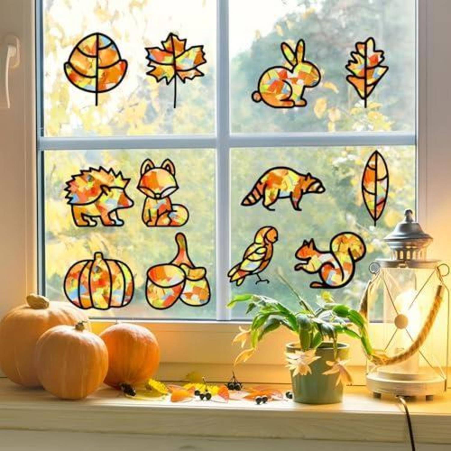 Herbstliche Fensterszene mit bunten Blatt- und Tier-Sonnenfängerdekoration, Kürbissen auf der Fensterbank, einer Topfpflanze und einer beleuchteten Laterne.