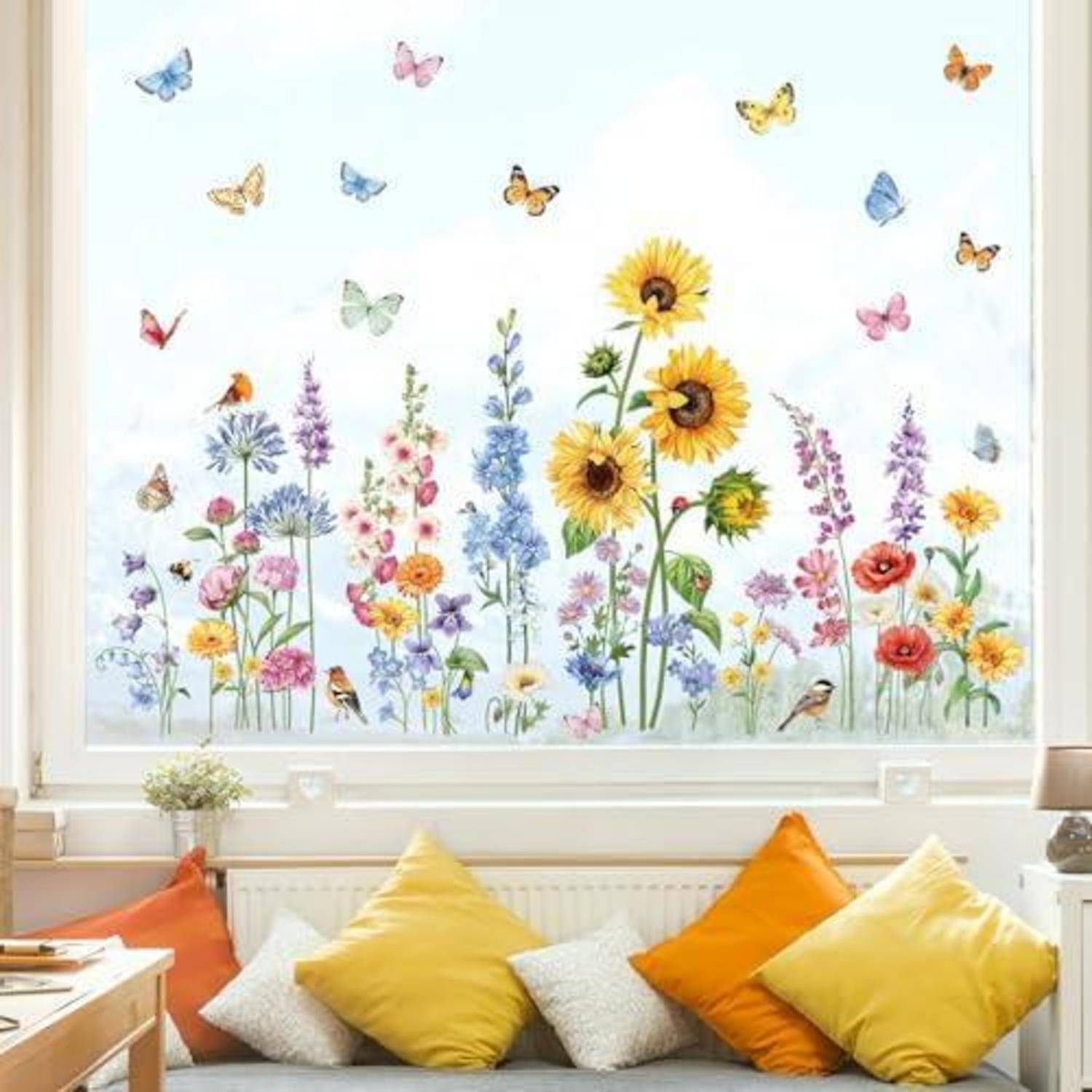 Ein helles Fenster-Wandgemälde mit farbenfrohen Wildblumen, Sonnenblumen, Schmetterlingen und Vögeln über einer Bank mit orangefarbigen und gelben Kissen.