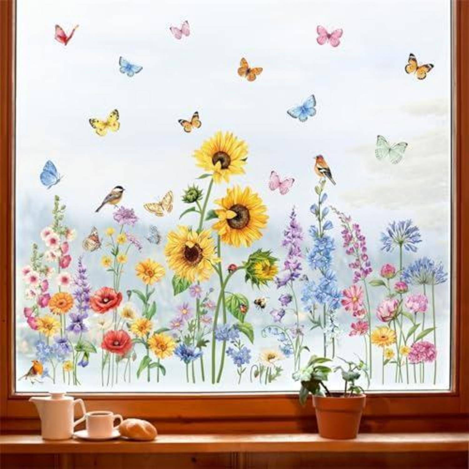 Sonnendurchflutetes Fenster mit einem farbenfrohen Blumengarten-Wandgemälde aus Sonnenblumen und Schmetterlingen, sichtbar über einer Fensterbank mit Topfpflanzen und Tassen.