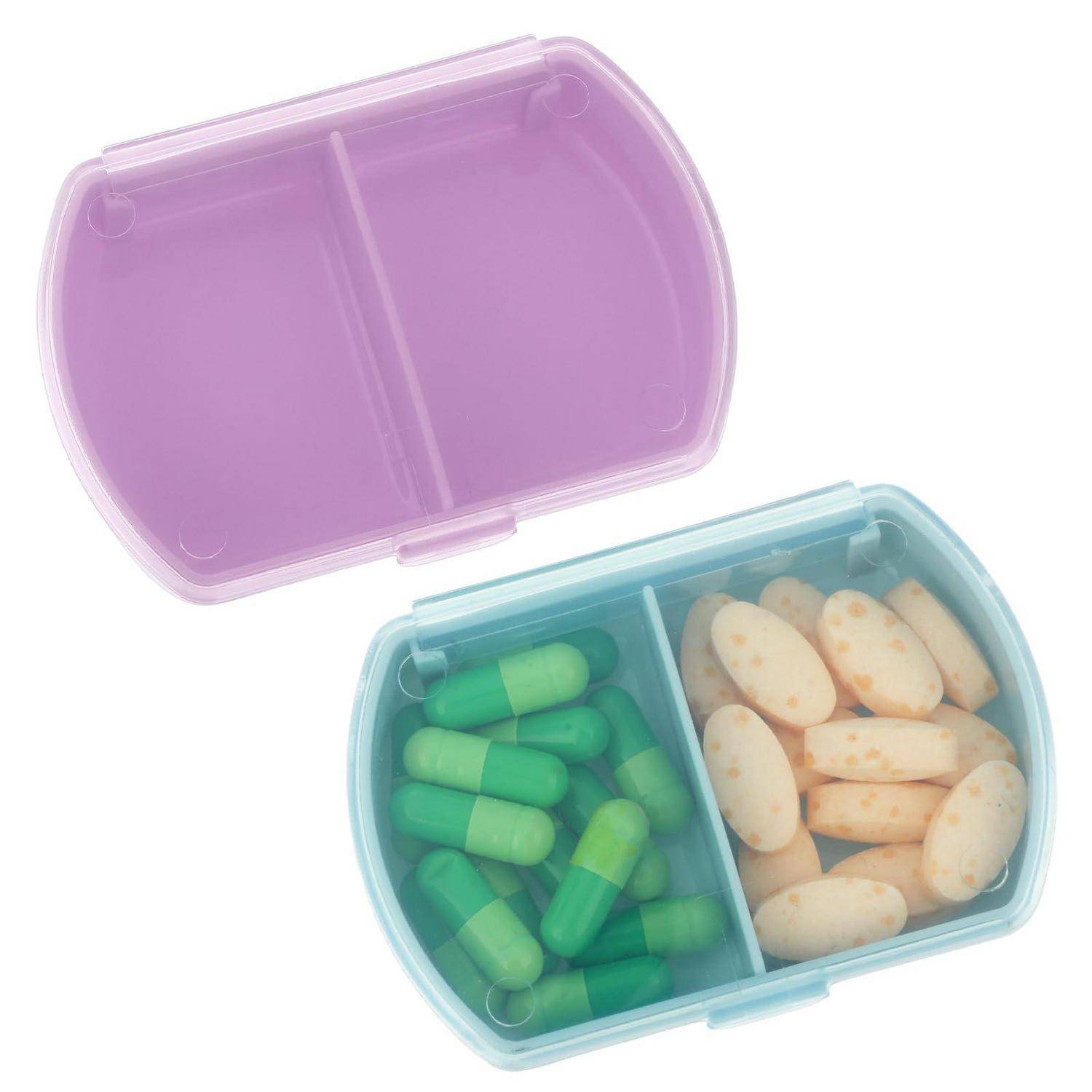 Offener durchsichtiger Pillorganizer mit zwei Fächern, gefüllt mit grünen Kapseln und beigen Tabletten, Deckel oben offen auf weißem Hintergrund