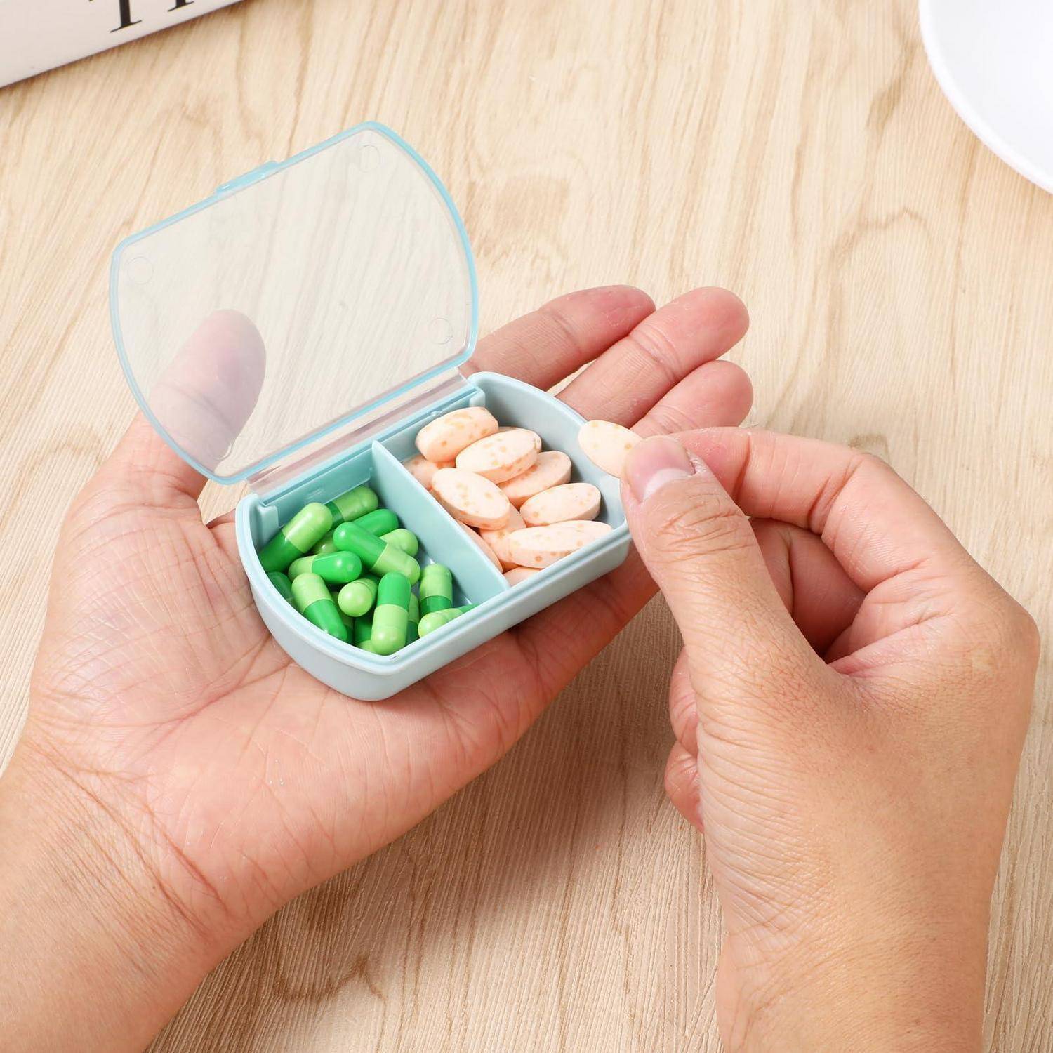 Hände halten einen kleinen mintgrünen Pillendispenser mit zwei Fächern, eines gefüllt mit grünen Kapseln und das andere mit pfirsichfarbenen Tabletten, auf einem Holztisch.