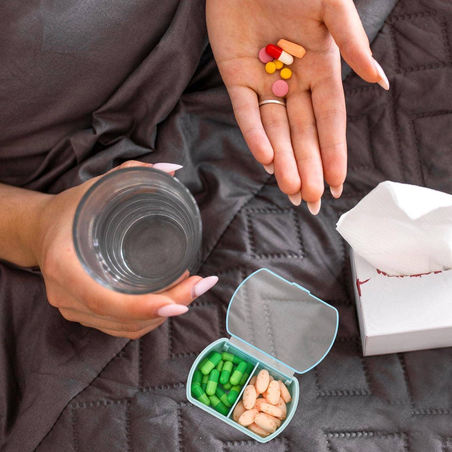 Eine Person hält verschiedene Pillen über einem Pillendosierer und einem Wasserglas, wobei eine offene Taschentuchbox in der Nähe zu sehen ist.