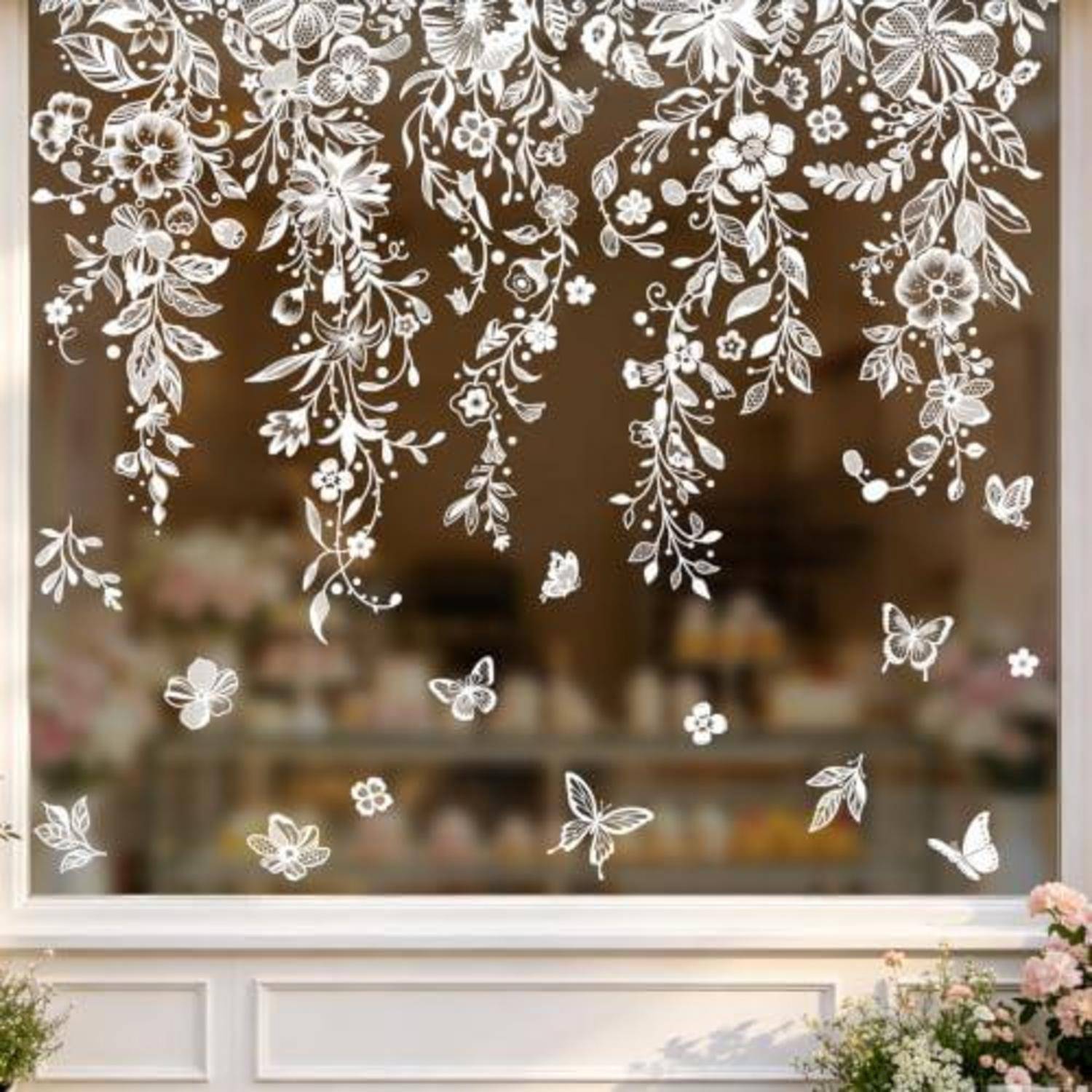 Fenster dekoriert mit weißen Blumen- und Schmetterlingsaufklebern, mit unscharfem Shopinneren hinter dem Glas sichtbar.