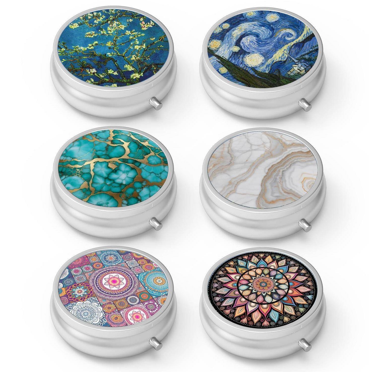 Sechs runde silberne Kompaktkästen mit unterschiedlichen dekorativen Deckeldesigns: Blütenzweige, Sternennacht-ähnlicher Himmel, türkissteín, Marmor, buntes Mosaik und Mandala.