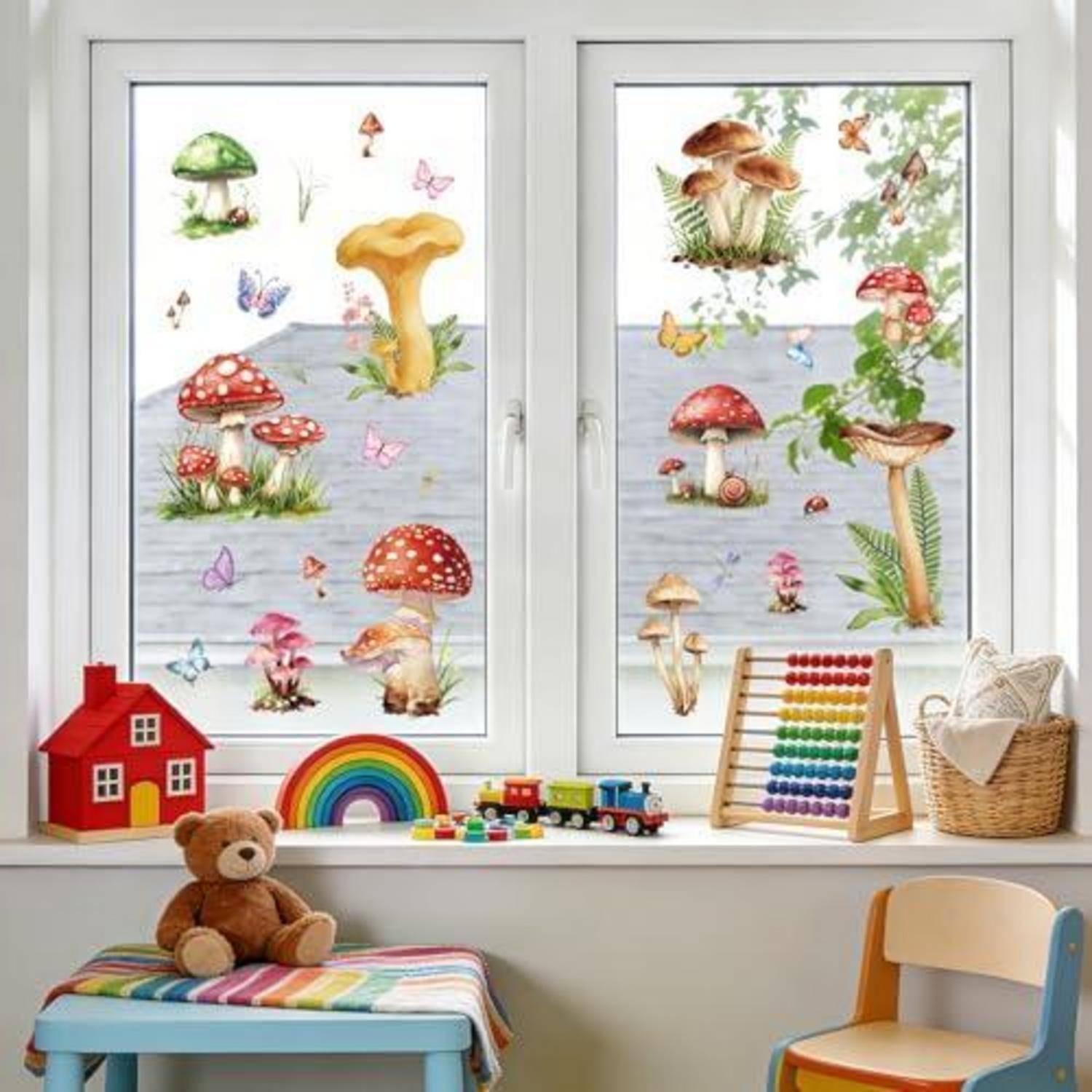 Kinderzimmerfenster mit Pilz- und Schmetterlingsaufklebern, Spielhaus, Regenbogen, Teddybär, Bauklötzen, Abakus und Korb auf einer Fensterbank.