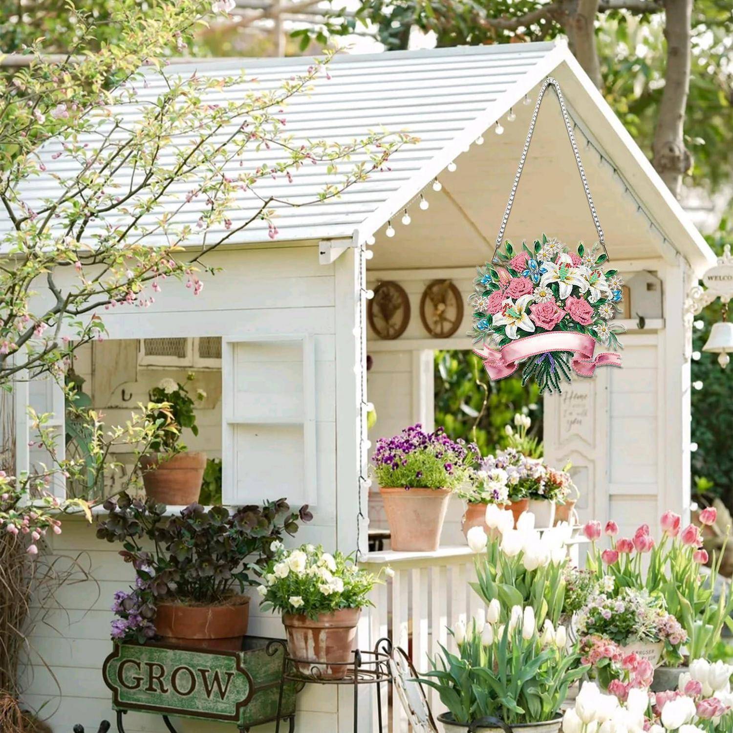 Ein dekoriertes weißes Gartenhaus mit Blumentöpfen, einem hängenden Blumenkranz und dem Wort „GROW" auf einem Blumenkübel, umgeben von blühenden Tulpen und Grünpflanzen.