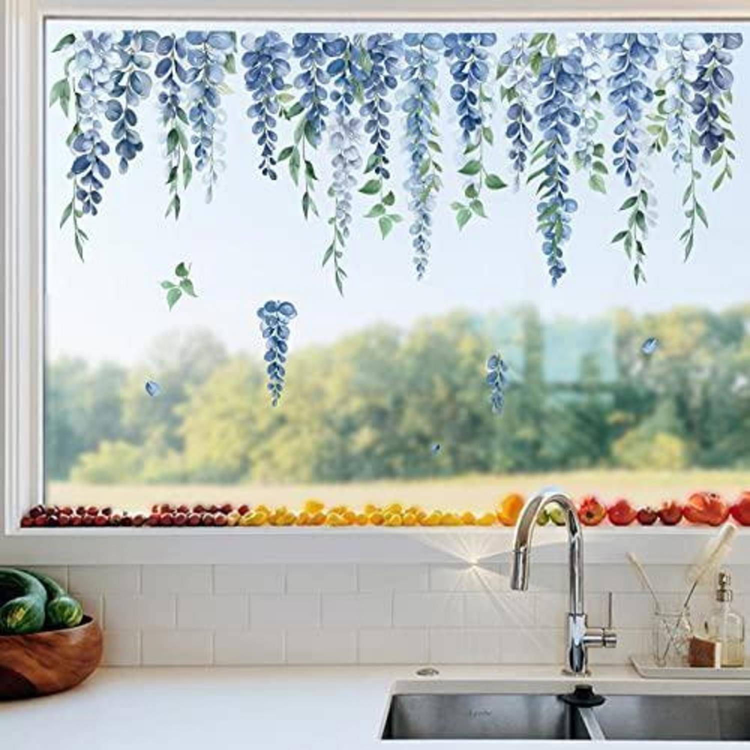 Küchenspüle unter einem Fenster, dekoriert mit hängenden blauen Blumengirlanden und bunten fruchtähnlichen Akzenten entlang der Fensterbank, mit Gartenblick nach außen.