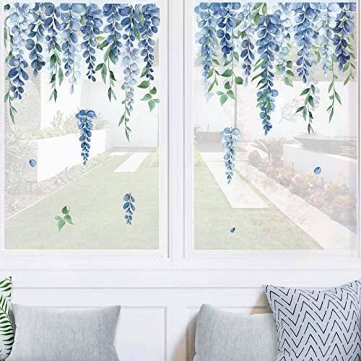 Fenster mit blauen und grünen hängenden Blumenaufklebern, die das Glas über einem Wohnzimmersofa und Kissen dekorieren.