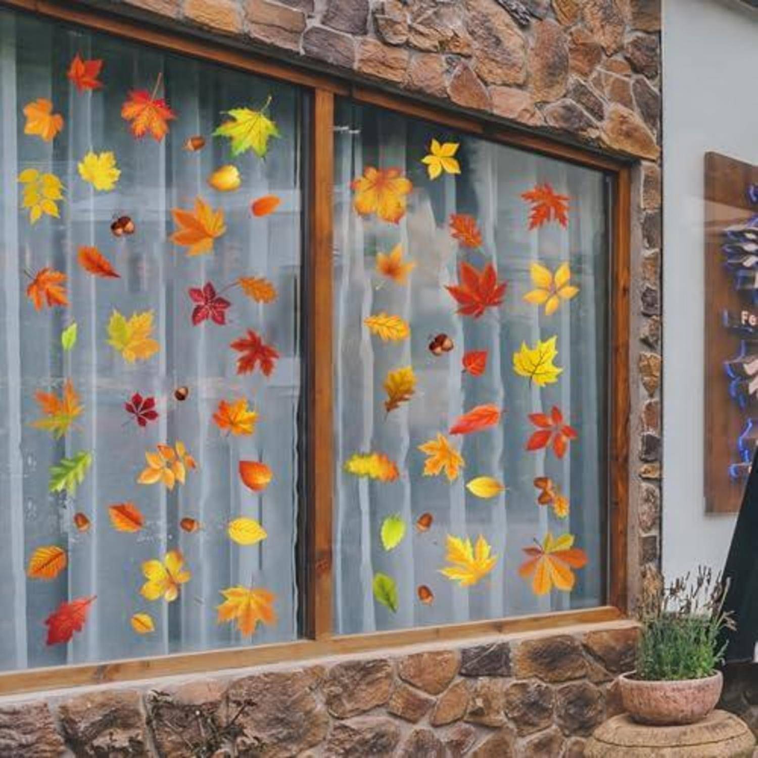 Steinerne Schaufensterfront mit bunten Papierlaub dekoriert, wobei ein herbstlich gestaltetes Display hinter durchsichtigen Vorhängen entsteht.