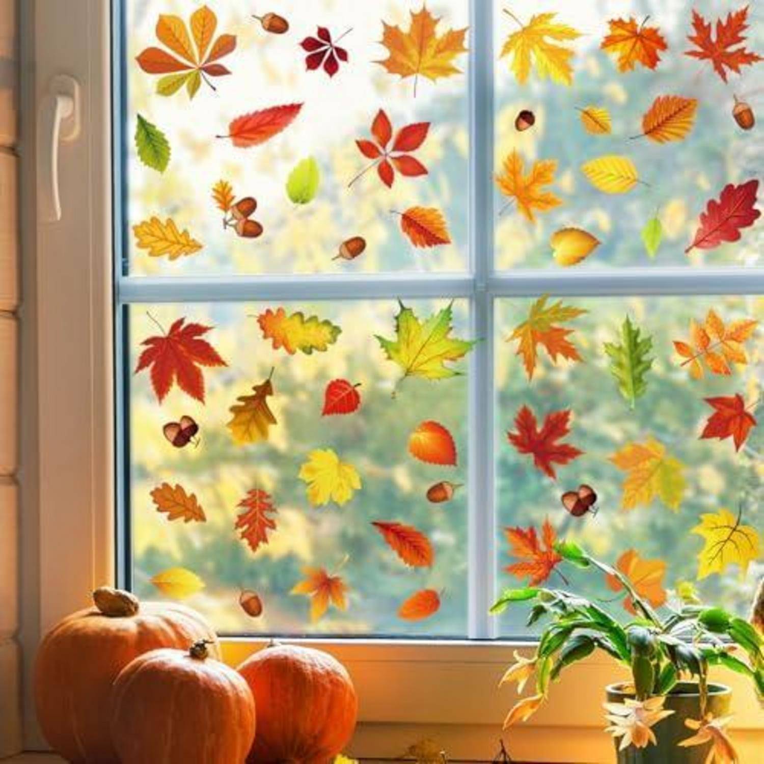 Herbstlich gestaltetes Fenster mit farbenfrohen Blattaufklebern, Kürbissen auf der Fensterbank und einer getopften Pflanze im warmen Sonnenlicht.