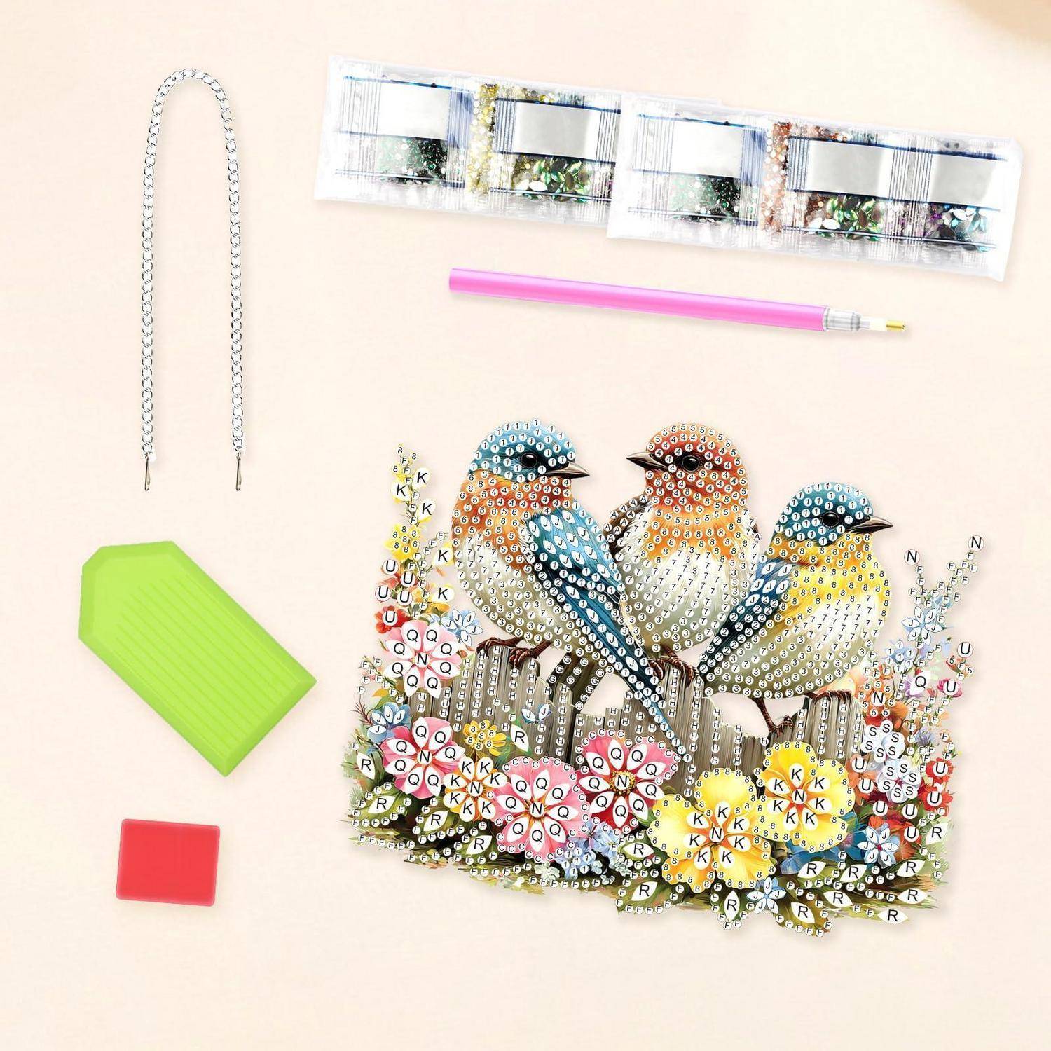 Diamantmalerei-Bastelset mit drei Vögeln auf Blumen, mit Werkzeugen und Materialien, die rund um das fertige Kunstwerk ausgebreitet sind.