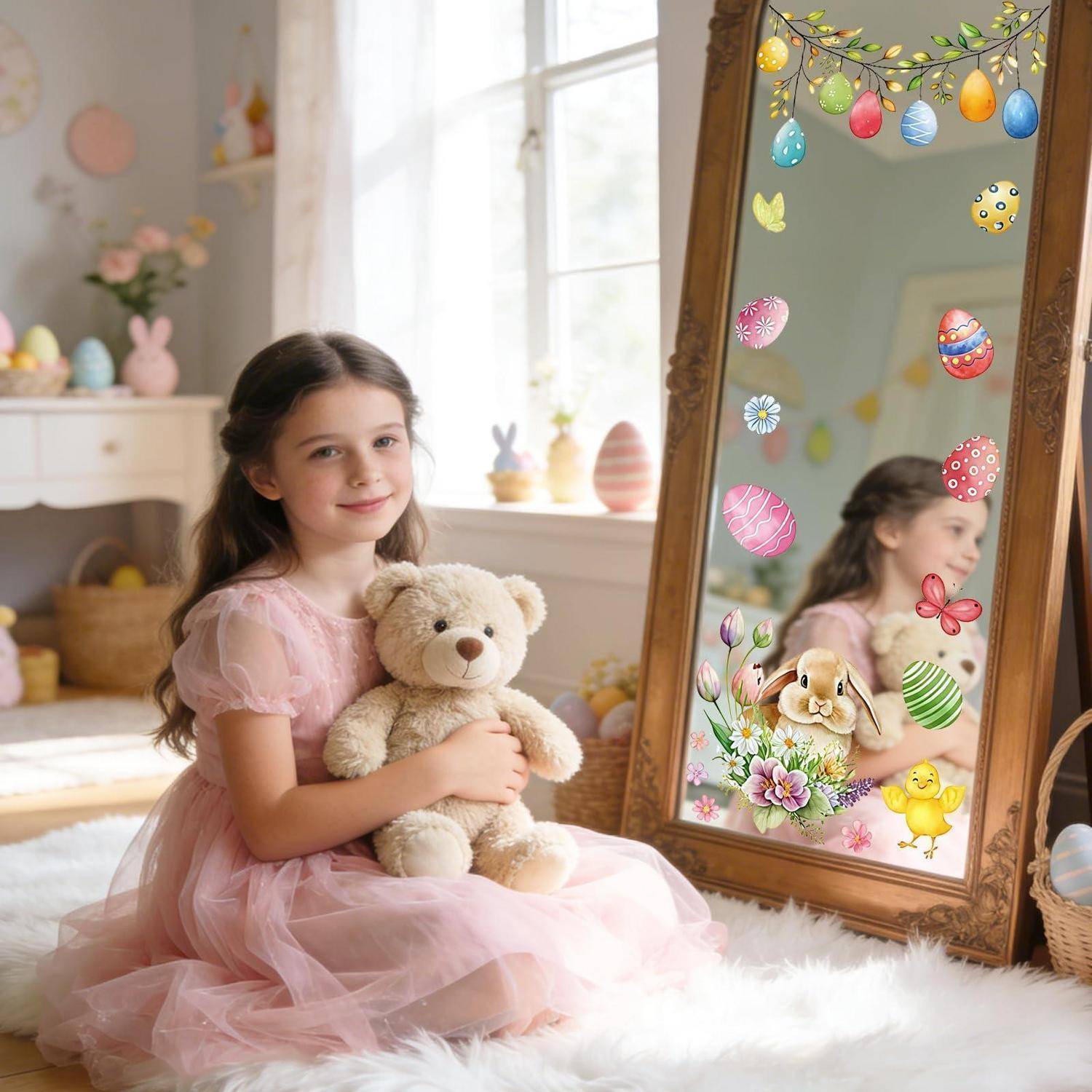 Ein junges Mädchen in einem rosa Kleid sitzt und hält einen Teddybären neben einem verzierten Spiegel mit Ostereiern und Blumenstickern in einem hellen Zimmer.