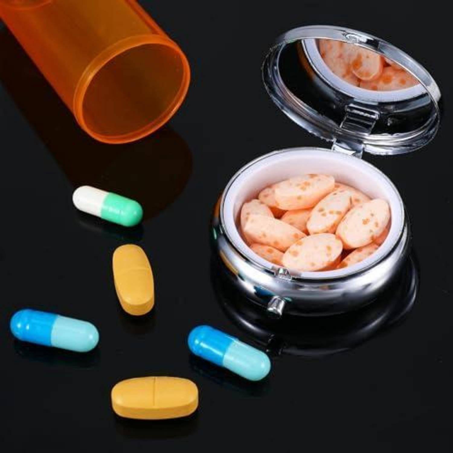 Verschiedene Pillen und Kapseln verstreut sich neben einer offenen Pillenflakone mit orangefarbenen Tabletten auf dunklem Hintergrund.