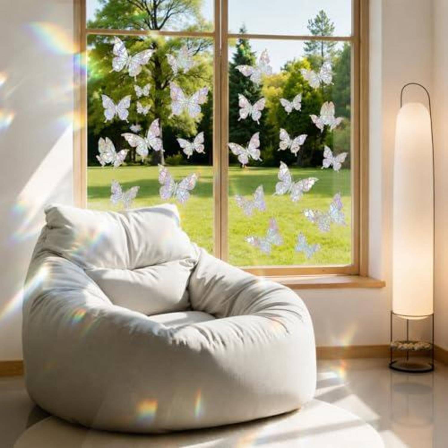 Weißer Sitzsack in einem sonnendurchfluteten Zimmer neben einer Stehleuchte, mit Schmetterlingsaufklebern am Fenster mit Blick auf einen grünen Hof.